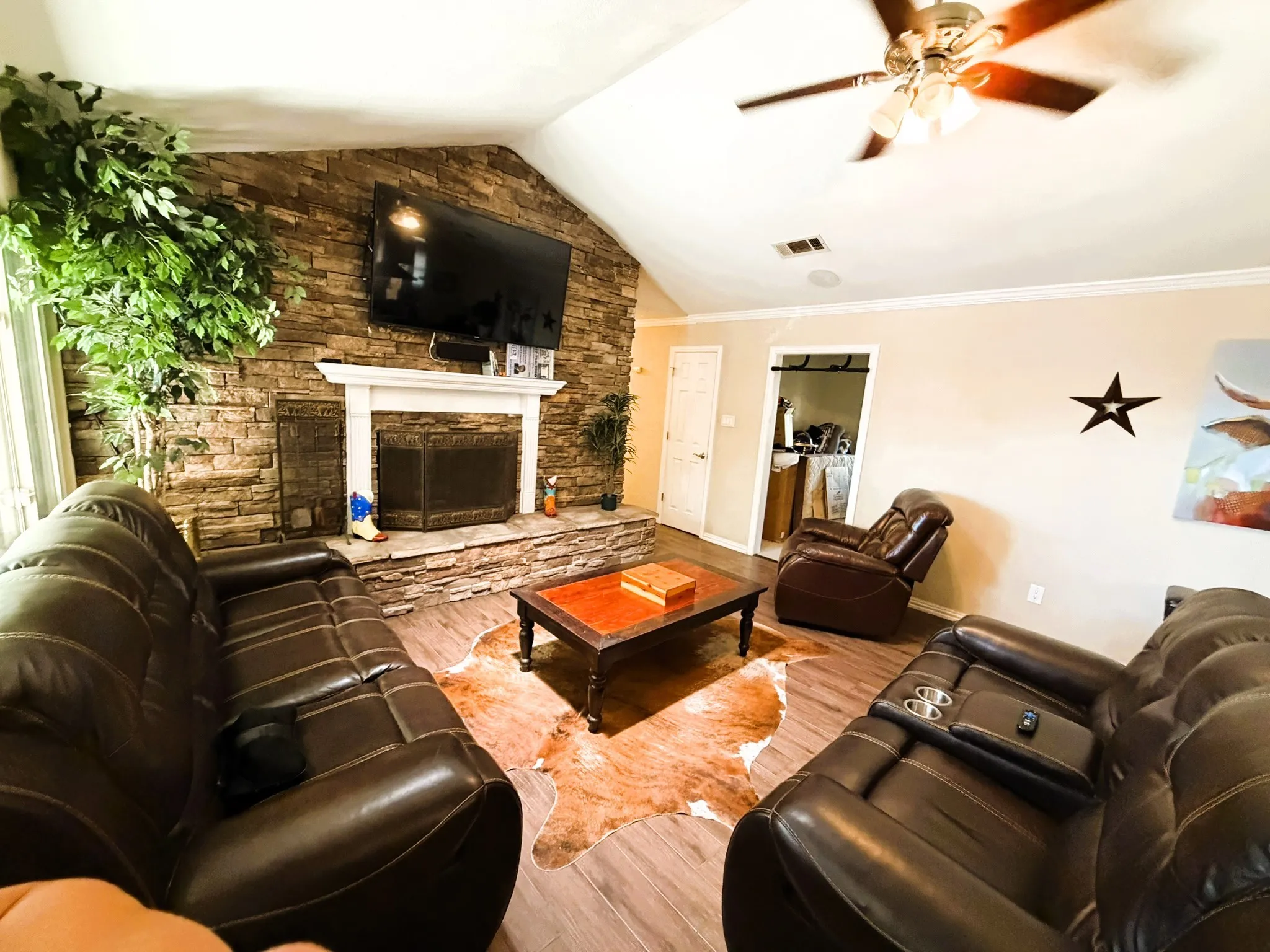 Vaulted ceiling with a ceiling fan, stone-clad fireplace, white mantel, and wood-finish flooring