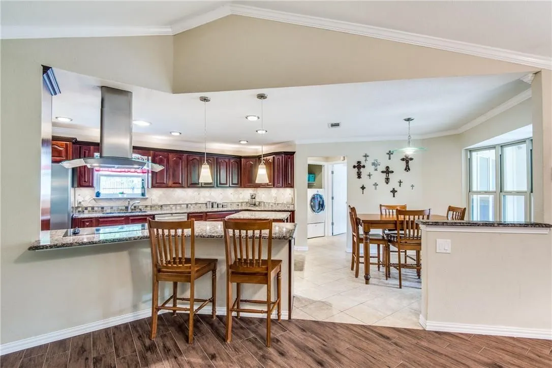 Kitchen featuring dark wood cabinetry, stainless steel range hood, recessed lighting, and a breakfast bar with stone countertops