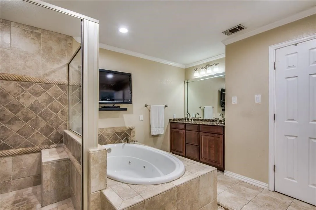 Tile-surround soaking tub, glass-enclosed shower with tiled bench, dual vanity with wood-finish cabinetry, and framed mirror