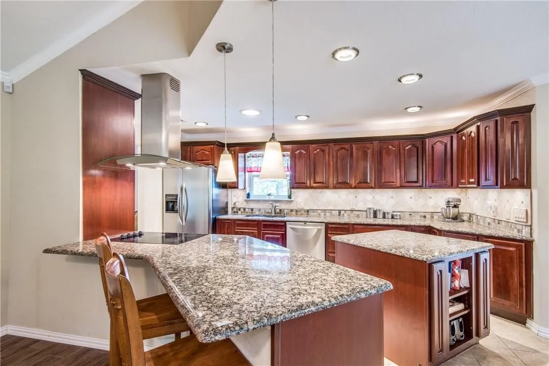 Kitchen featuring rich wood cabinetry, granite countertops, a central island, recessed lighting, and stainless steel appliances