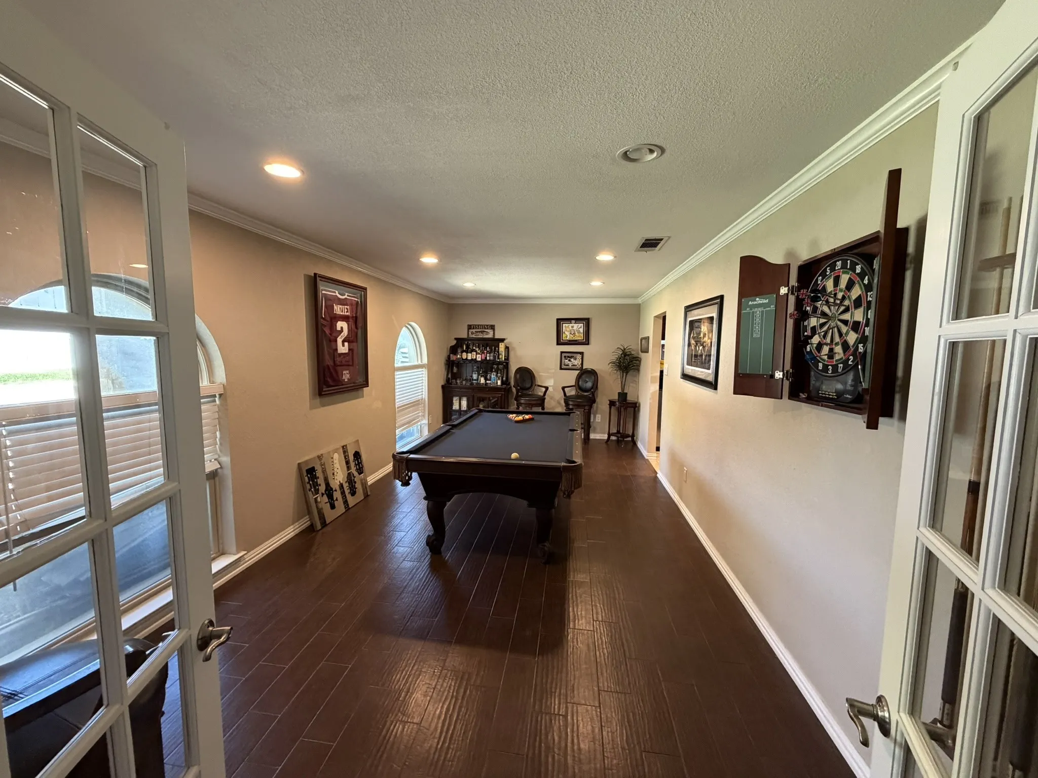Wood-finish flooring, recessed lighting, crown molding, arched windows, and white French doors