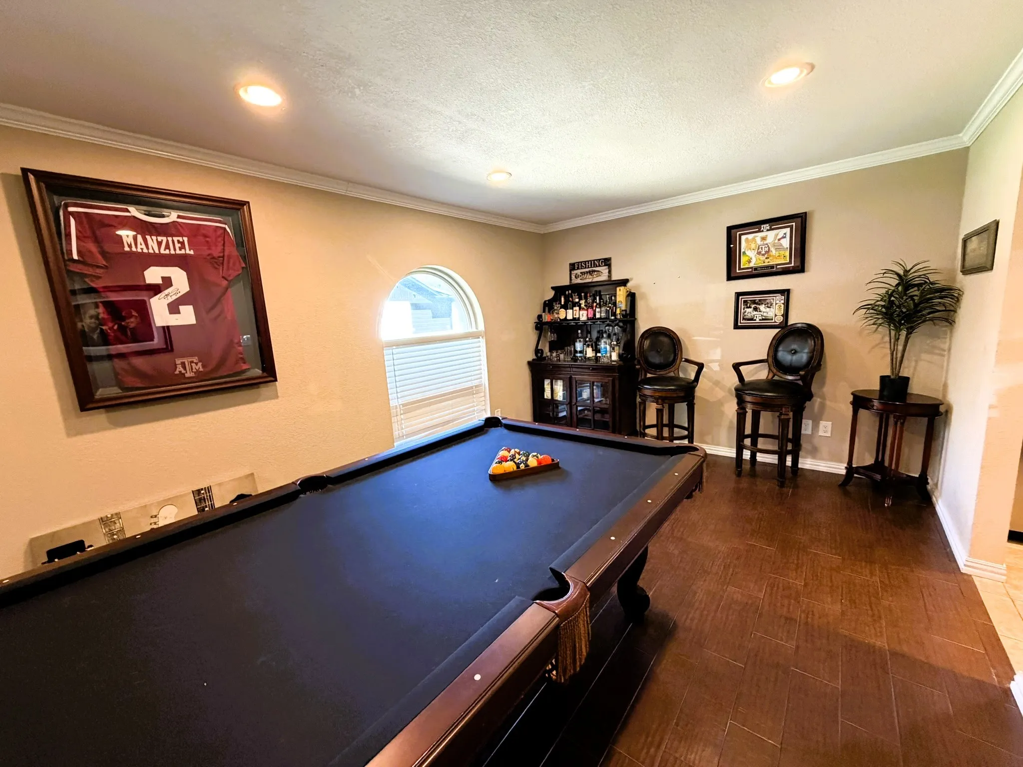 Recessed ceiling lighting, crown molding, wood-finish flooring, arched window, and built-in bar cabinet