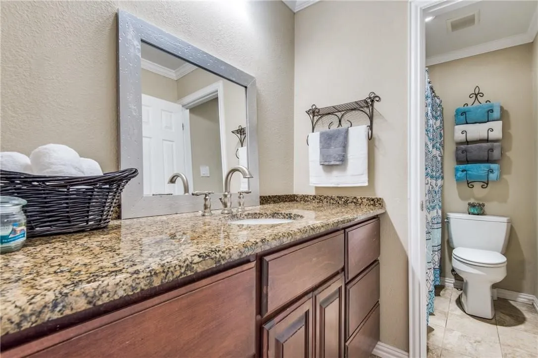 Granite countertop, wood-finish cabinetry, and a framed vanity mirror