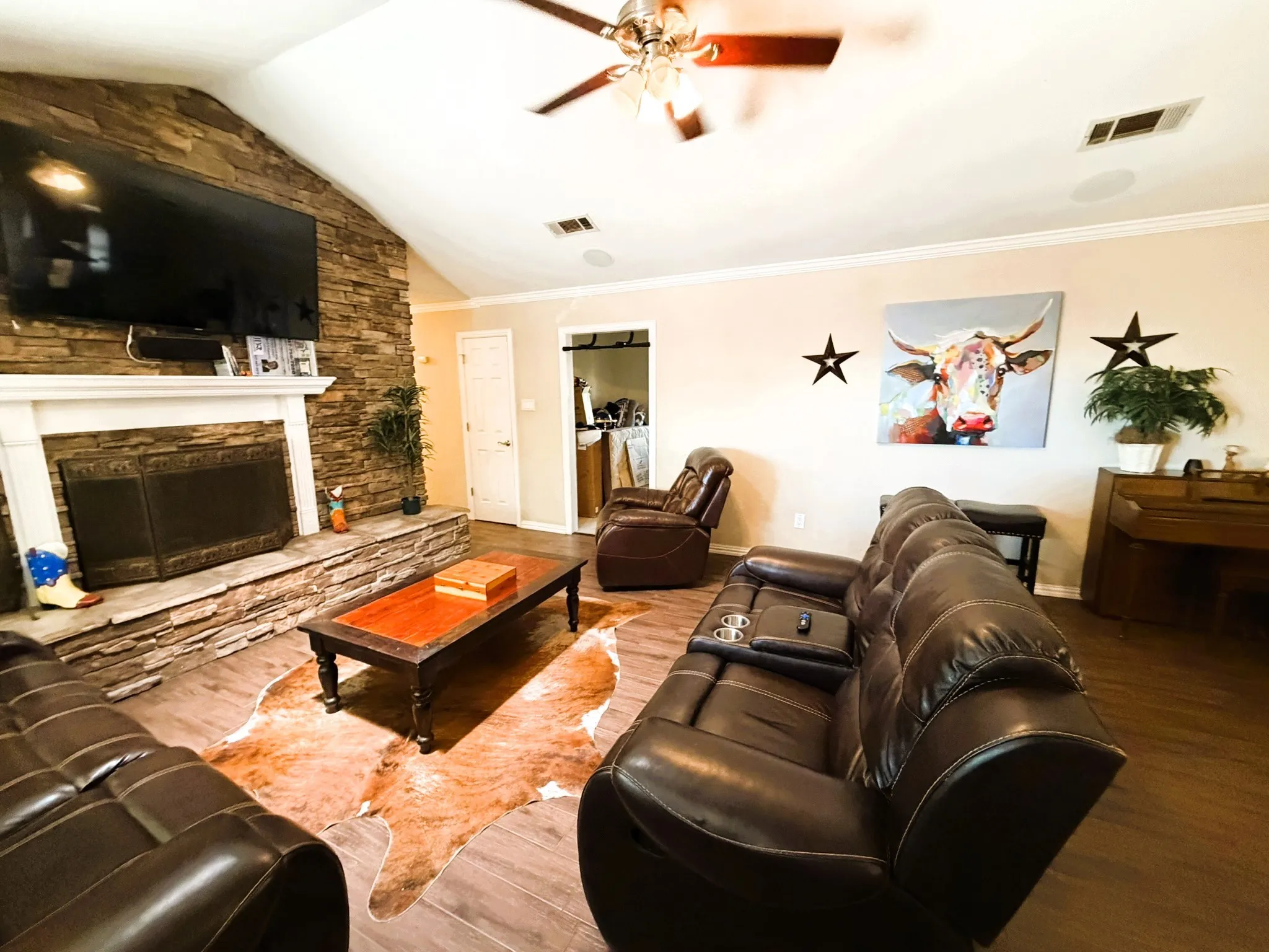 Vaulted ceiling with a ceiling fan, stone-clad fireplace with mantel, and wood-finish flooring
