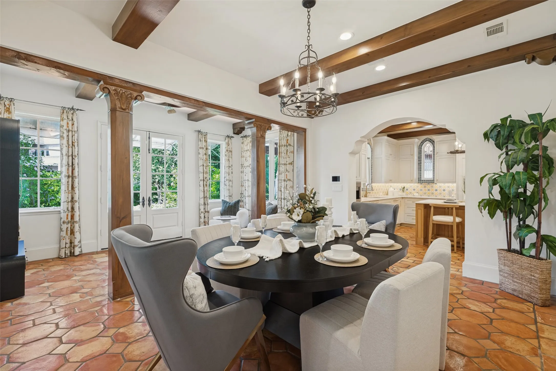 Exposed wood ceiling beams, terra cotta-style flooring, a wrought iron chandelier, carved wood support columns, and an arched entryway