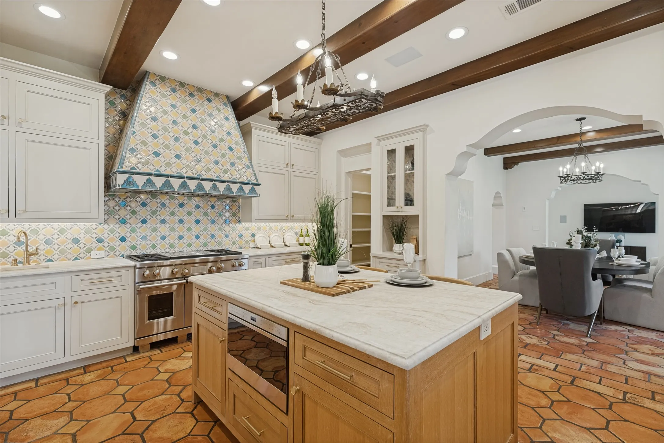 Gourmet kitchen featuring a tile-front range hood, stainless steel professional-grade range, custom cabinetry, large island with integrated microwave, and wood-beam ceiling accents