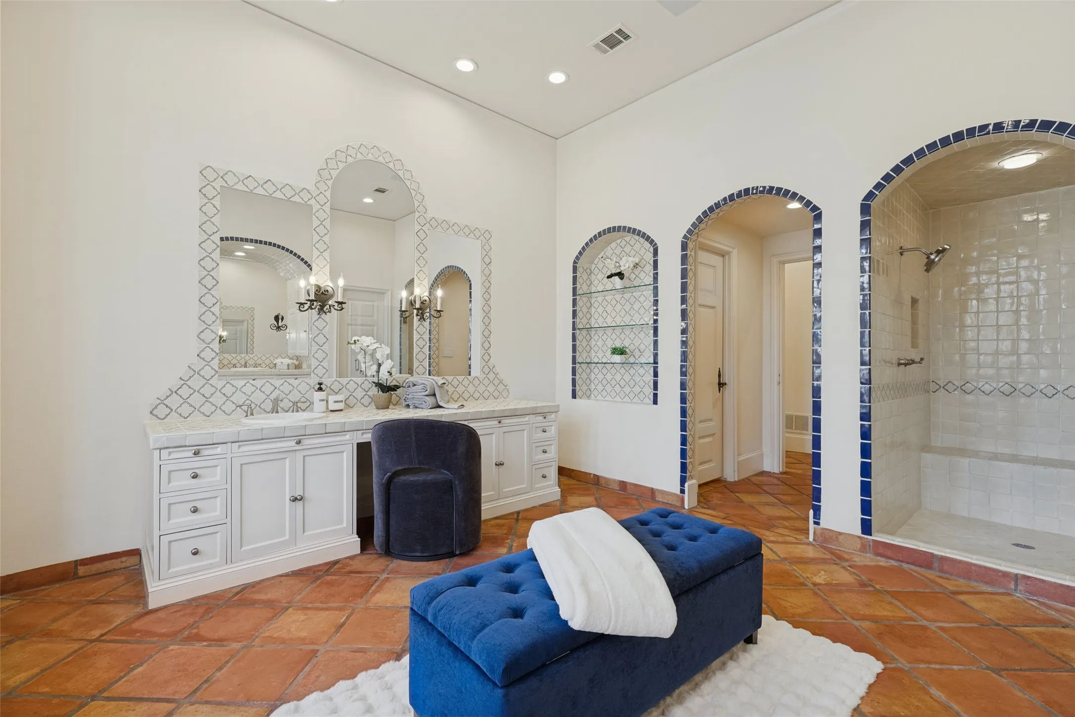 Tile flooring, dual vanities with integrated sinks, decorative mirror surrounds, arched doorways, and a walk-in shower with tile accents