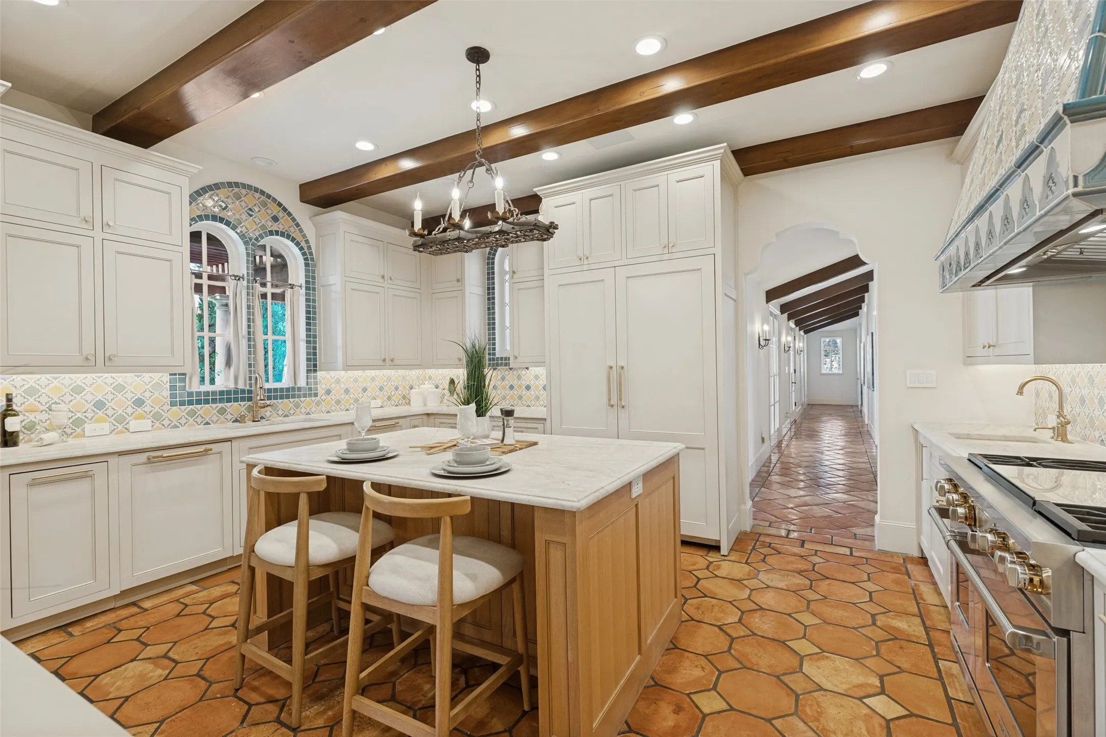 Custom kitchen featuring exposed wood beams, hexagon terracotta tile flooring, white cabinetry, a center island with seating, and an arched entry