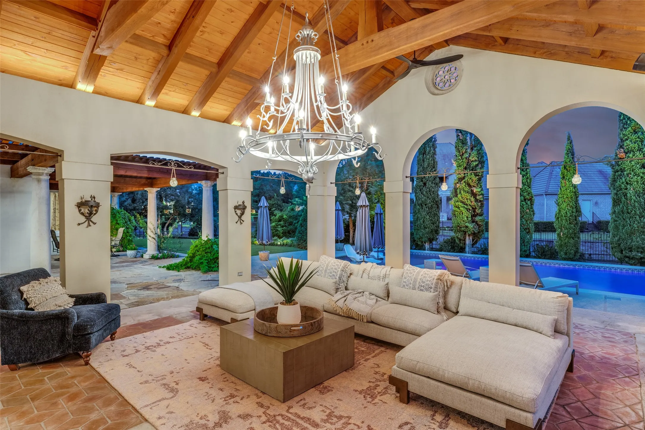Vaulted wood-beamed ceiling, arched openings, large chandelier, terracotta tile flooring, and a swimming pool