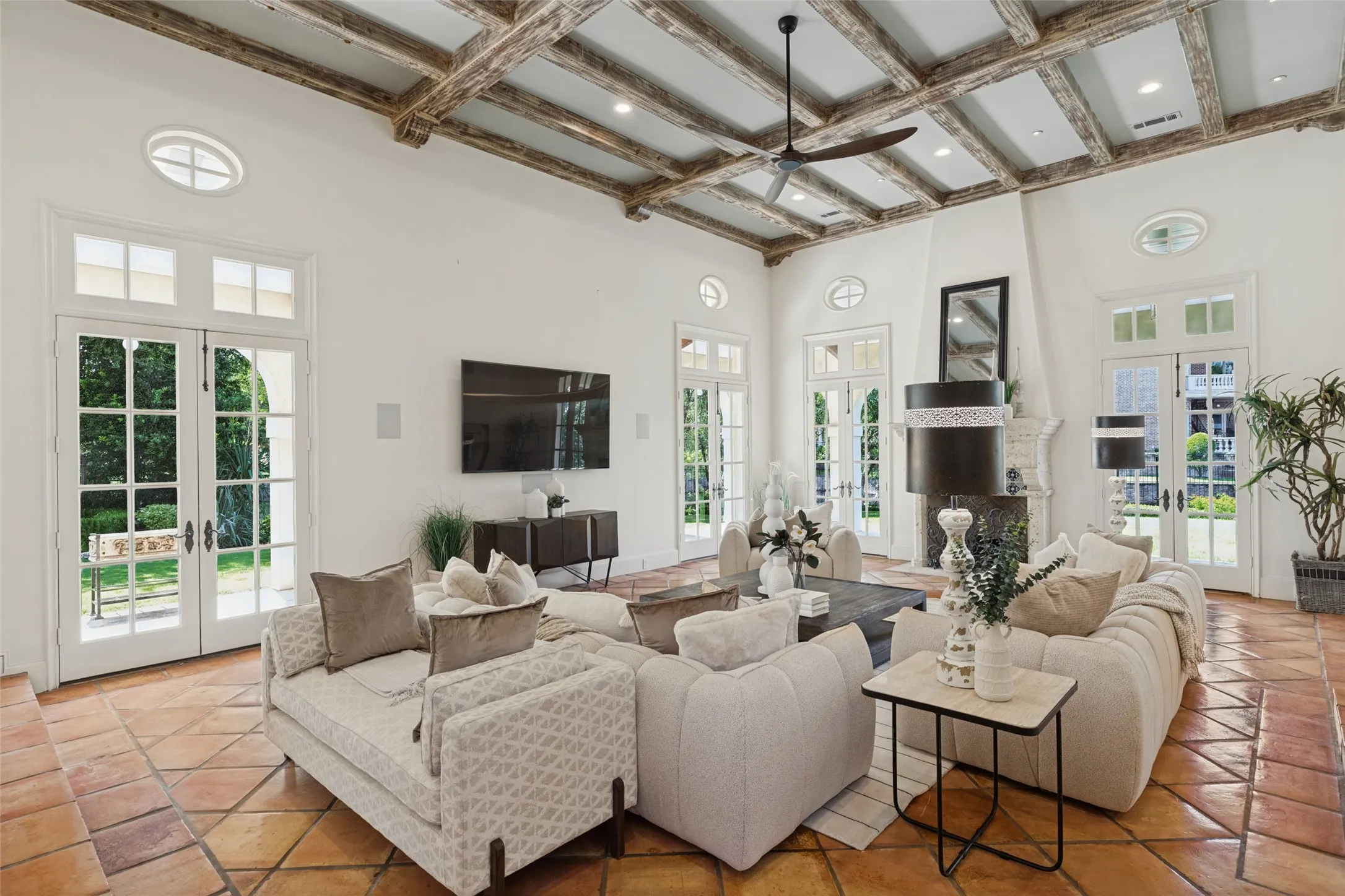 High ceilings with exposed wood beams, terracotta tile flooring, and multiple sets of French doors with transom windows
