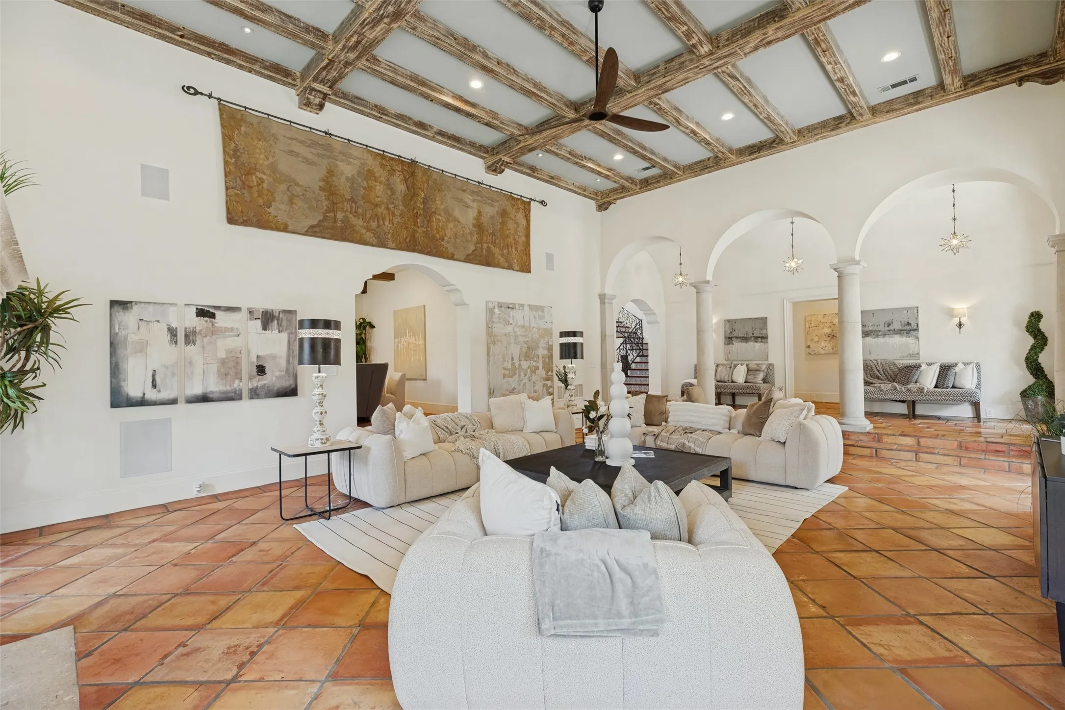 Expansive living area featuring a coffered wood-beam ceiling, terracotta tile flooring, arched doorways, and structural columns