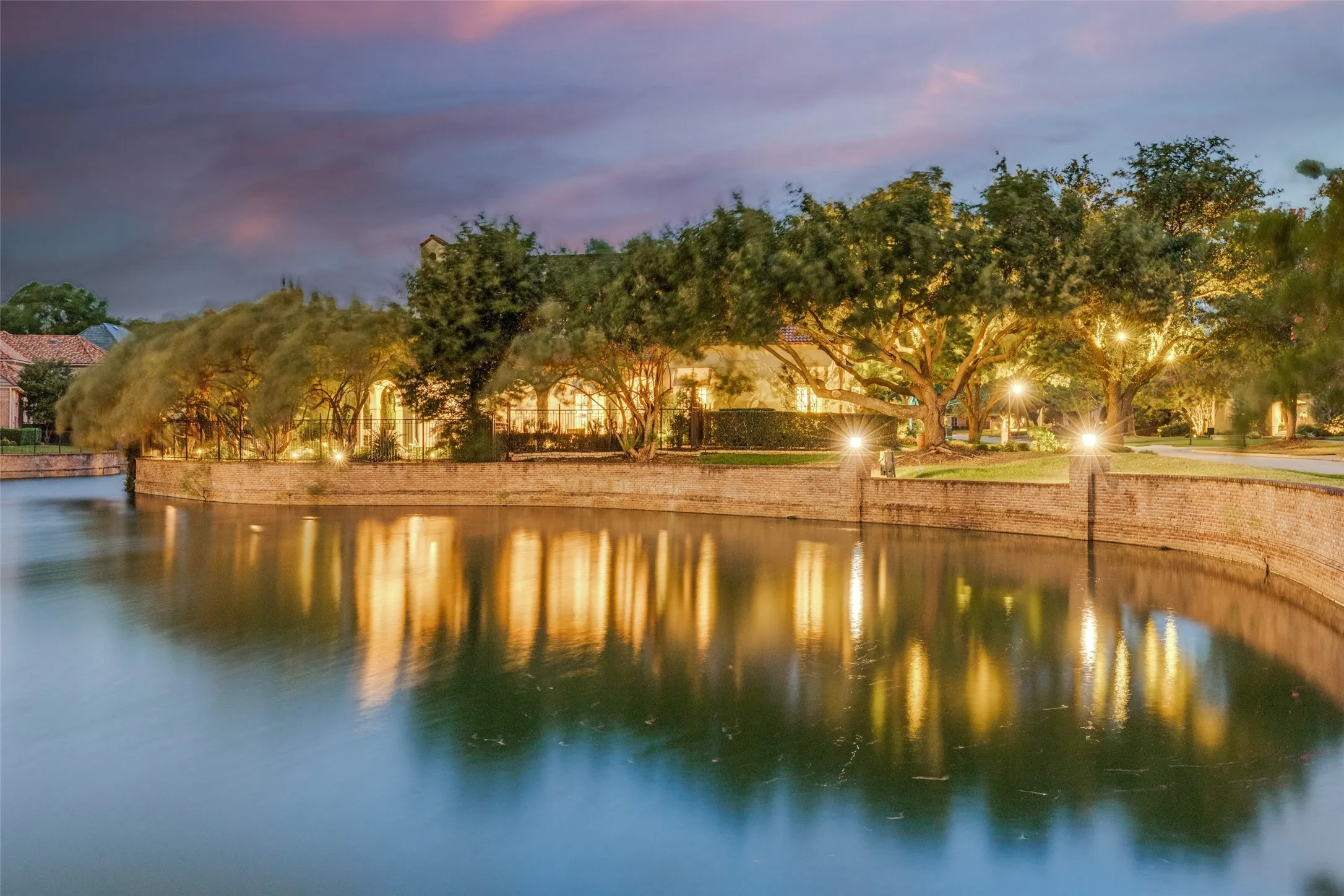 Waterfront property featuring mature trees and exterior illumination