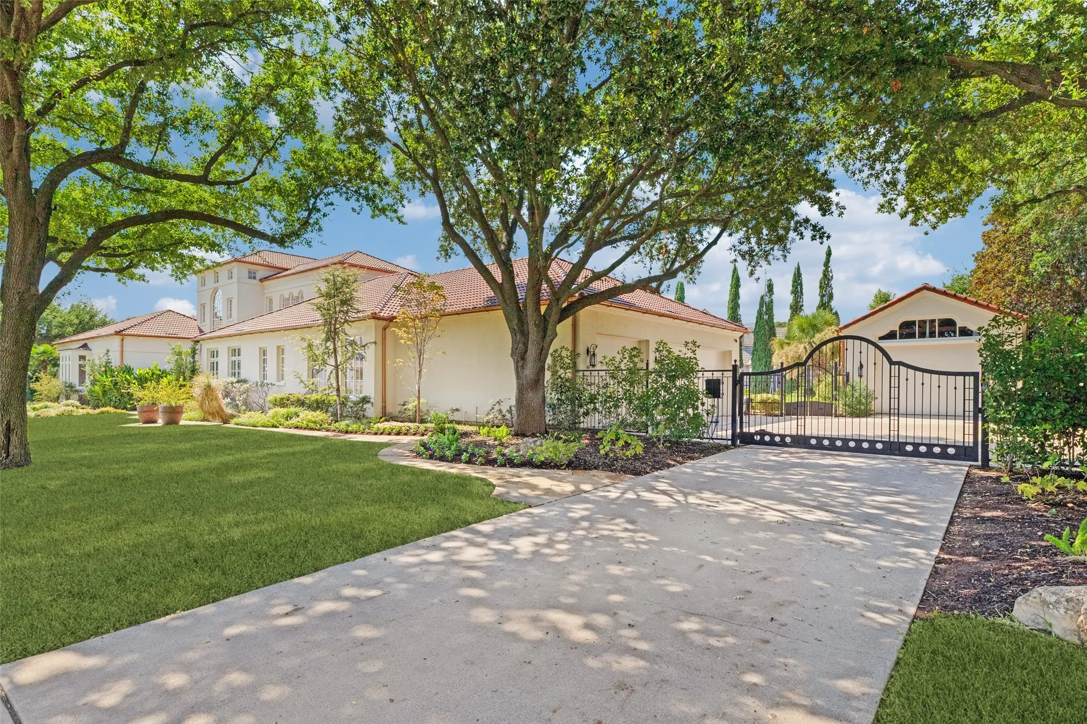 Elegant residence showcasing a gated entrance, circular driveway, and mature landscaping with established trees
