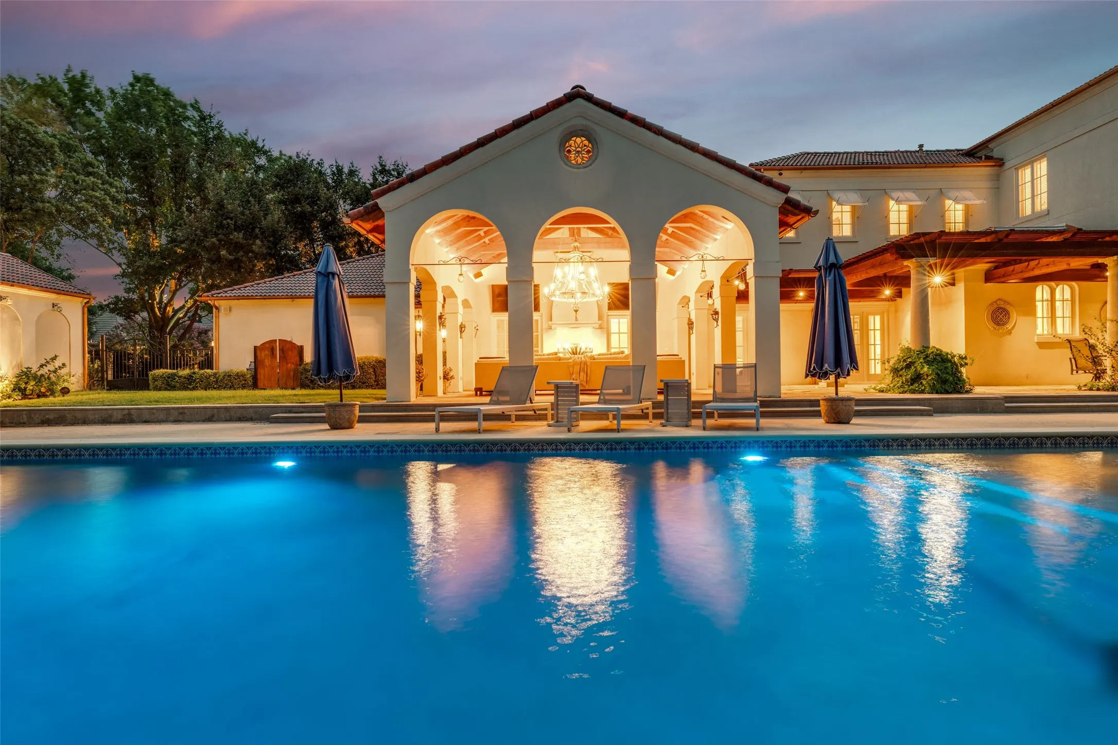Swimming pool with integrated lighting, covered patio with arched entries, red tile roofing, and an exterior wall finished in stucco