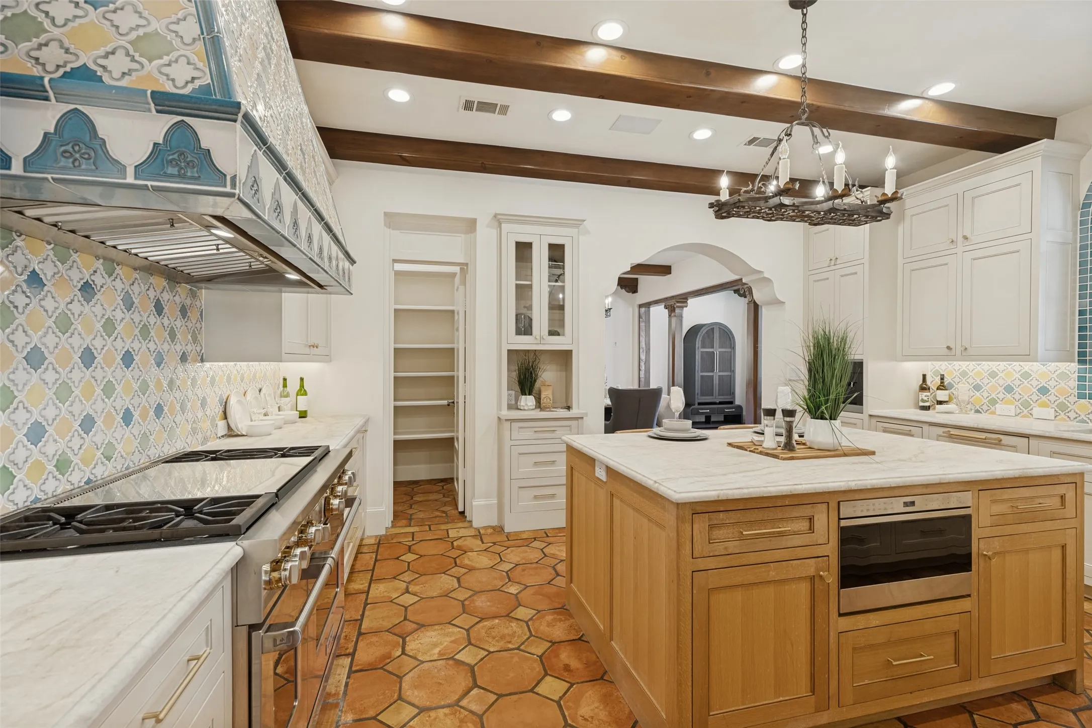 Exposed wood beams, decorative tile backsplash, wood-finish flooring, custom range hood, and a built-in kitchen island with integrated appliances