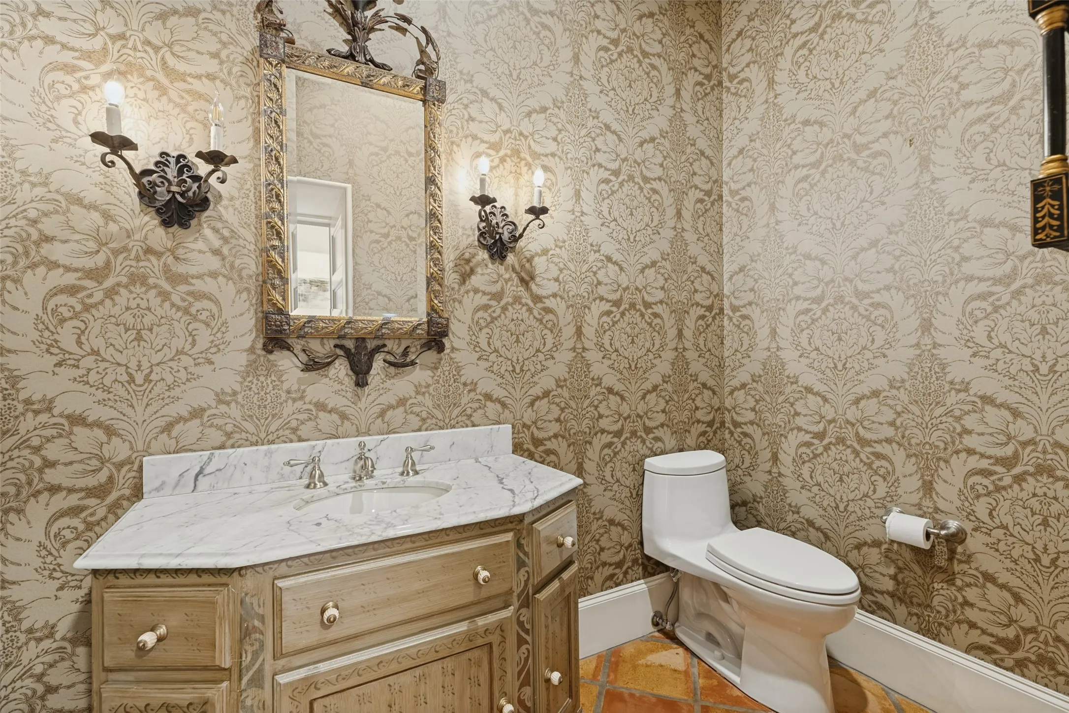 Ornate vanity with a light stone countertop, an undermount sink, and decorative sconces framing a framed mirror