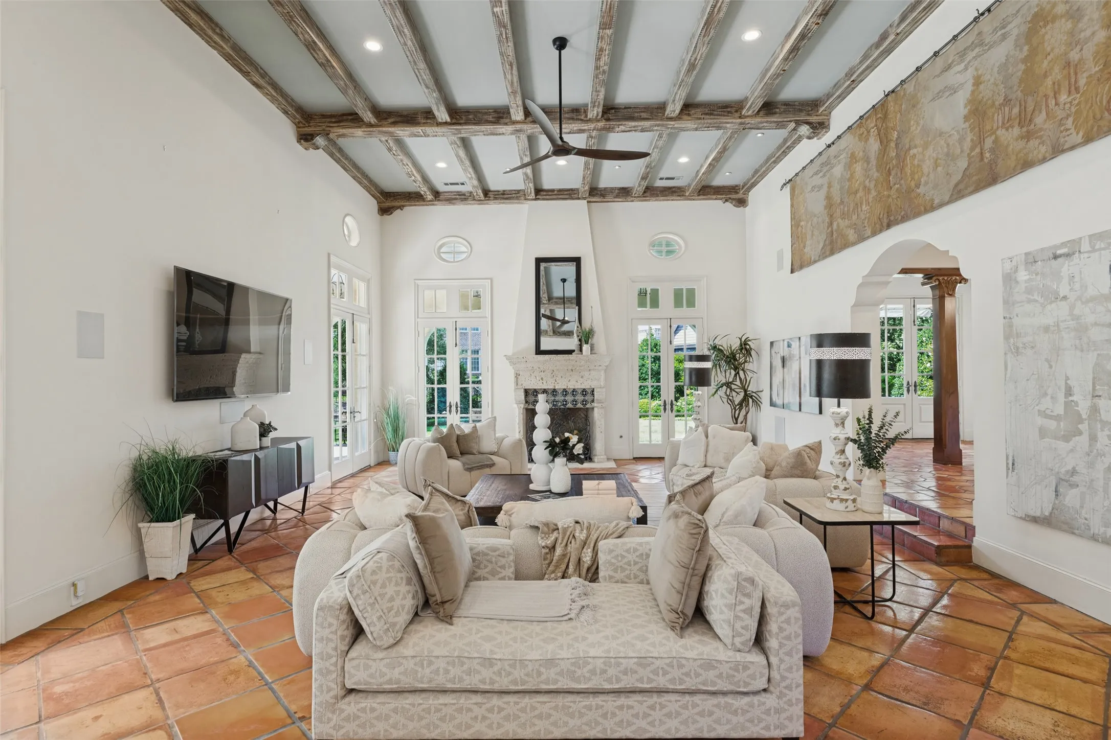 High ceilings with exposed wood beams, natural tile flooring, fireplace with ornate mantel, recessed lighting, and multiple sets of French doors