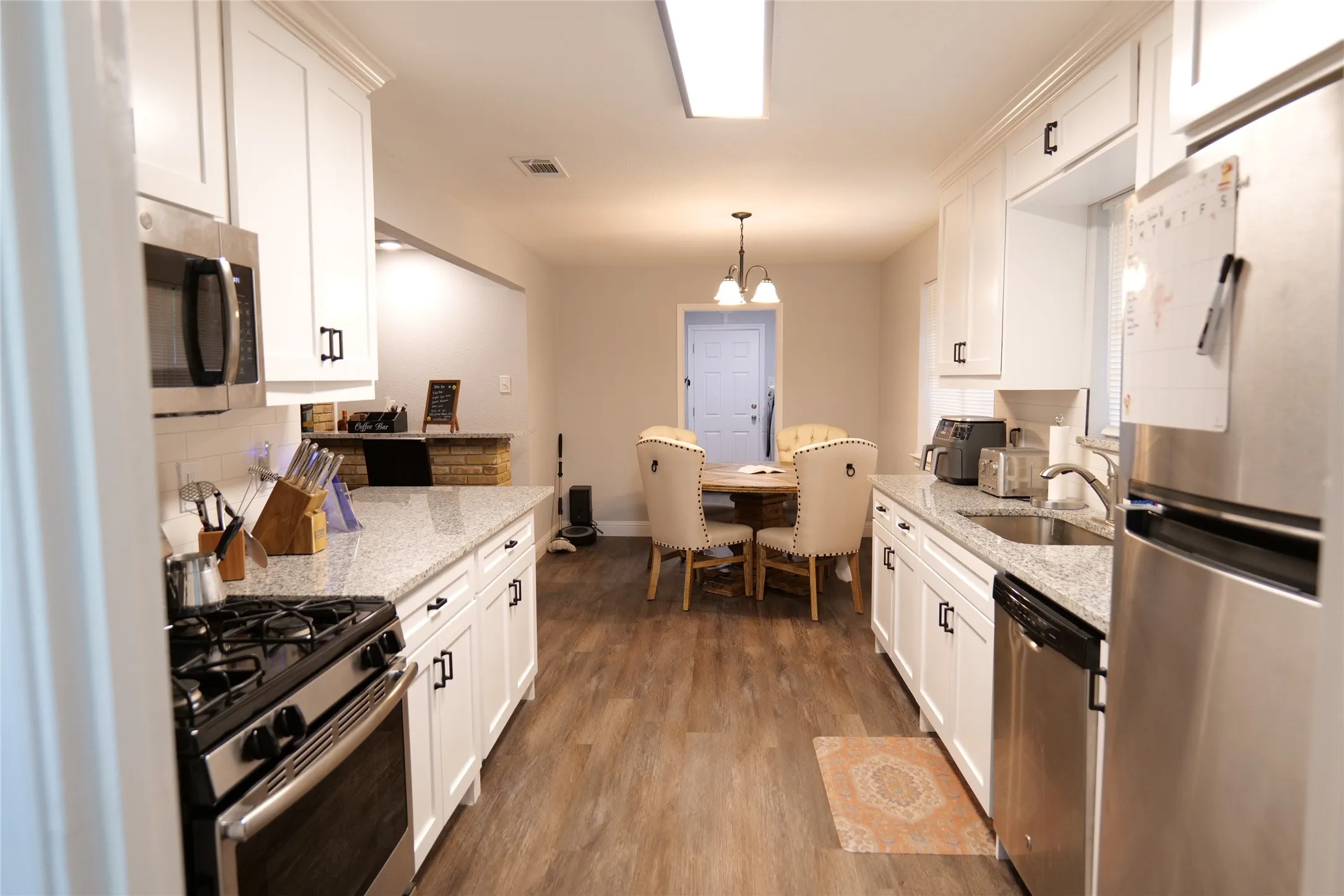 Galley kitchen featuring white cabinetry, light-toned countertops, stainless steel appliances, and wood-finish flooring