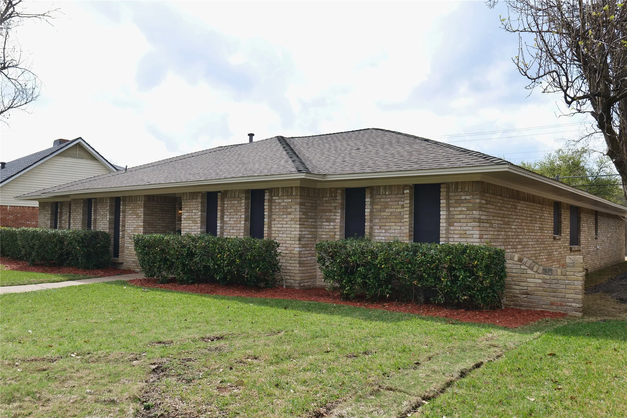 Brick exterior with a dark shingle roof, established landscaping, and a manicured lawn