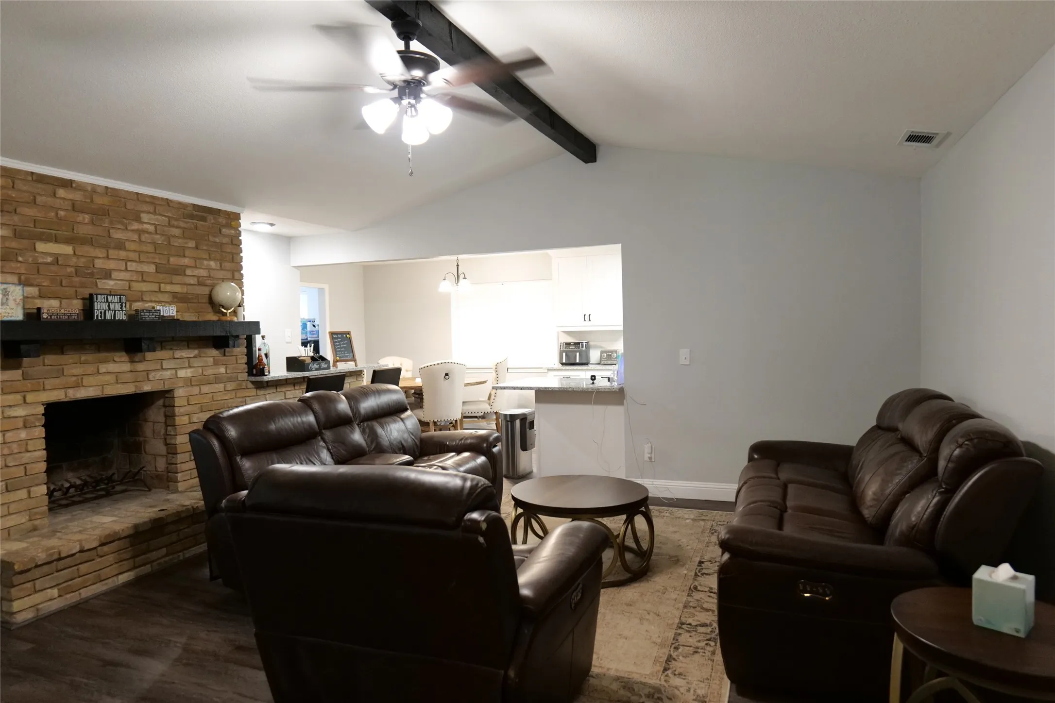 Vaulted ceiling with exposed beam, brick fireplace with mantel, wood-finish flooring, and recessed lighting