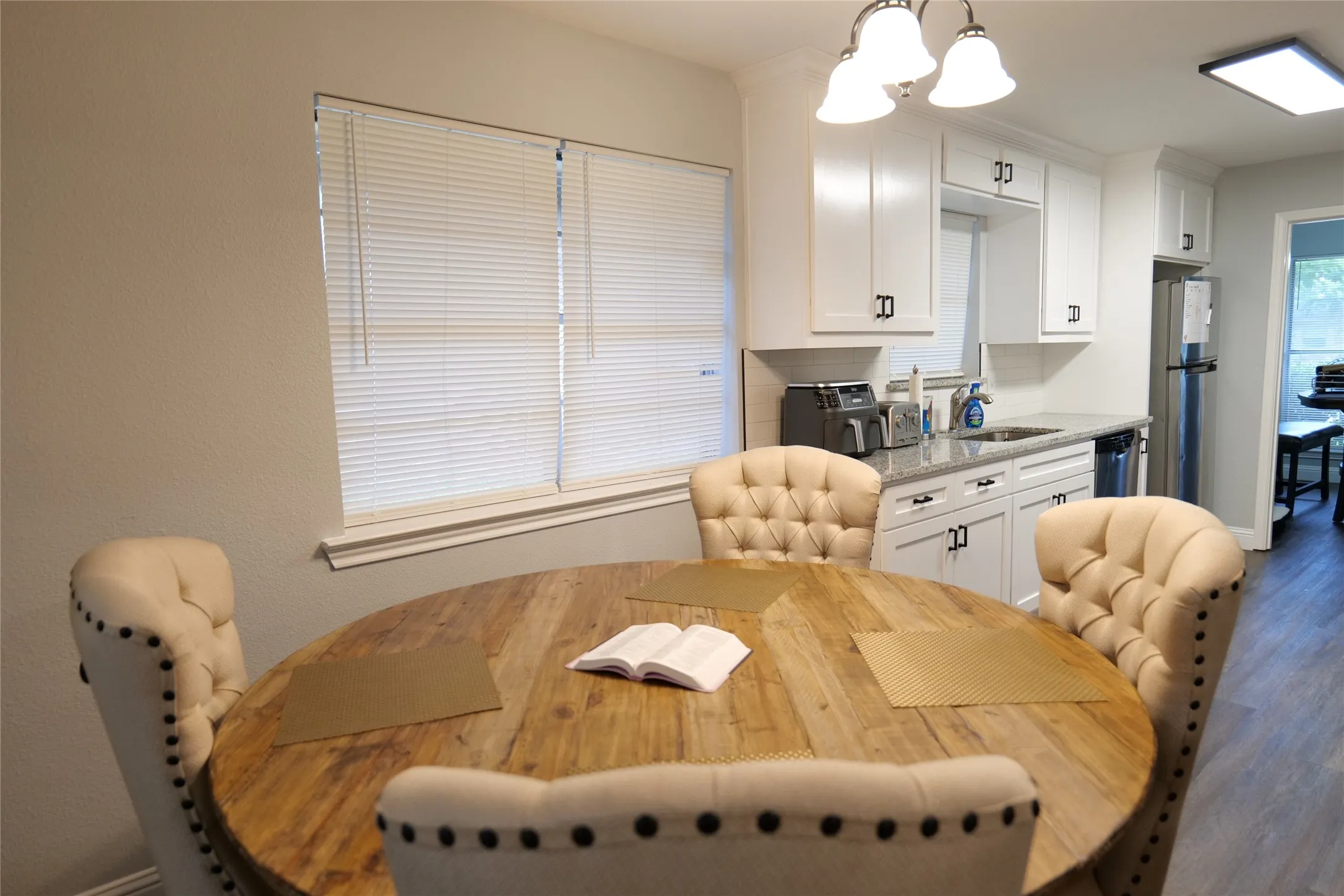 White shaker-style cabinetry with dark hardware, undermount sink, light-toned countertops, and wood-finish flooring