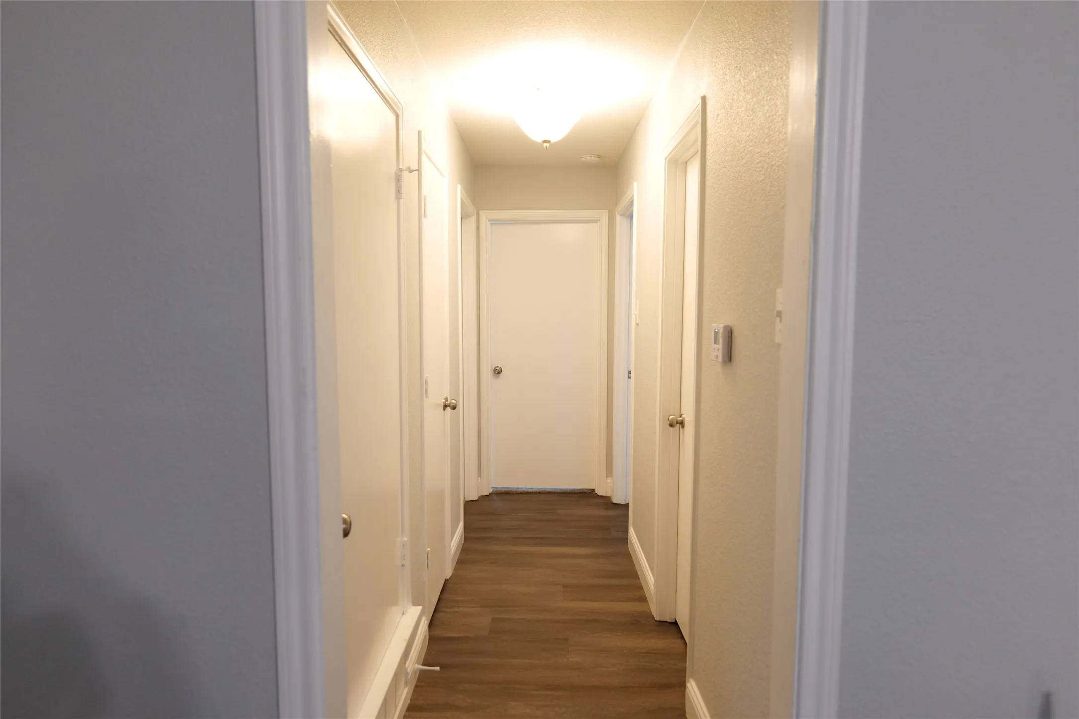 Hallway with wood-finish flooring, light gray walls, white trim, and multiple flush-mount light fixtures