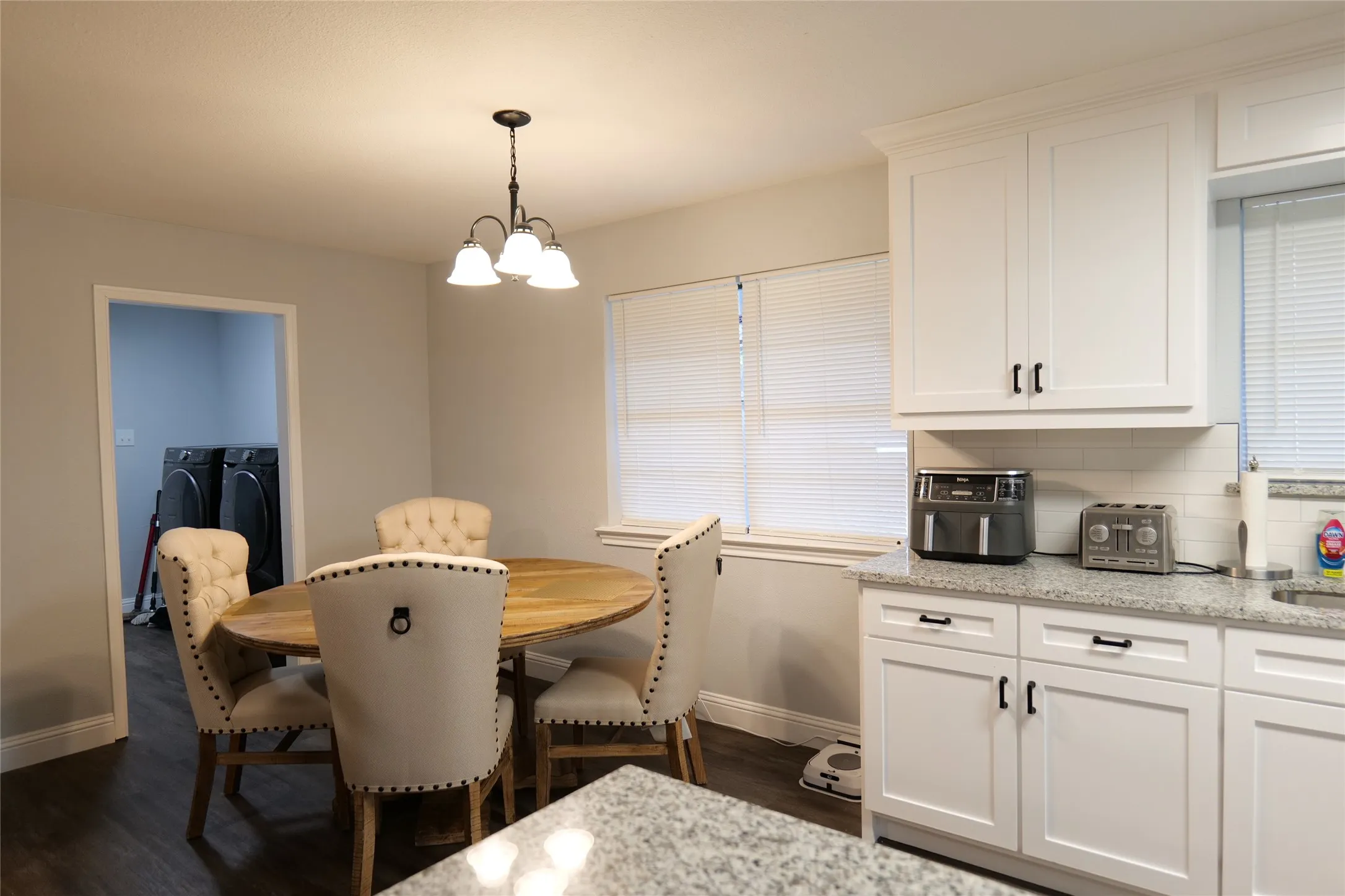 White shaker-style cabinetry, granite countertops, subway tile backsplash, wood-finish flooring, and a window with horizontal blinds