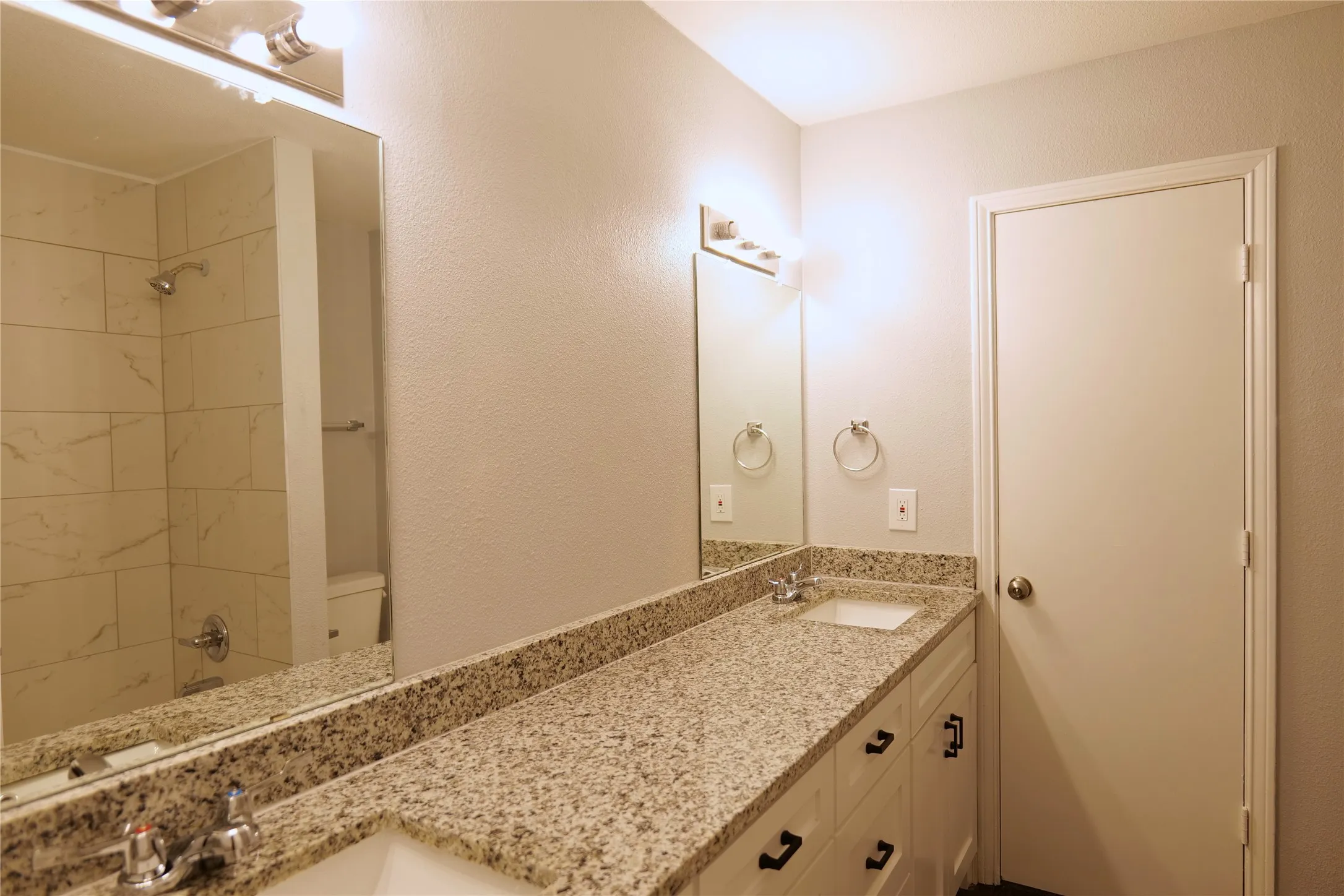 Dual vanity with granite-finish countertop, white cabinetry with black hardware, and undermount sinks