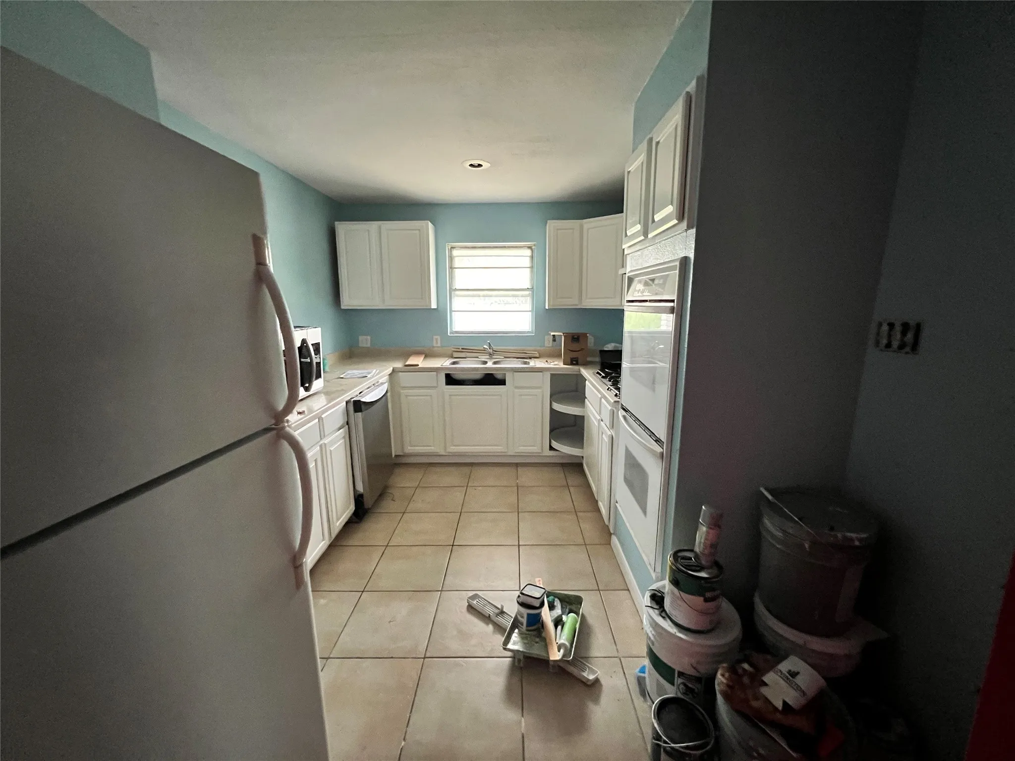 Kitchen featuring sink, white cabinets, light tile floors, and stainless steel appliances