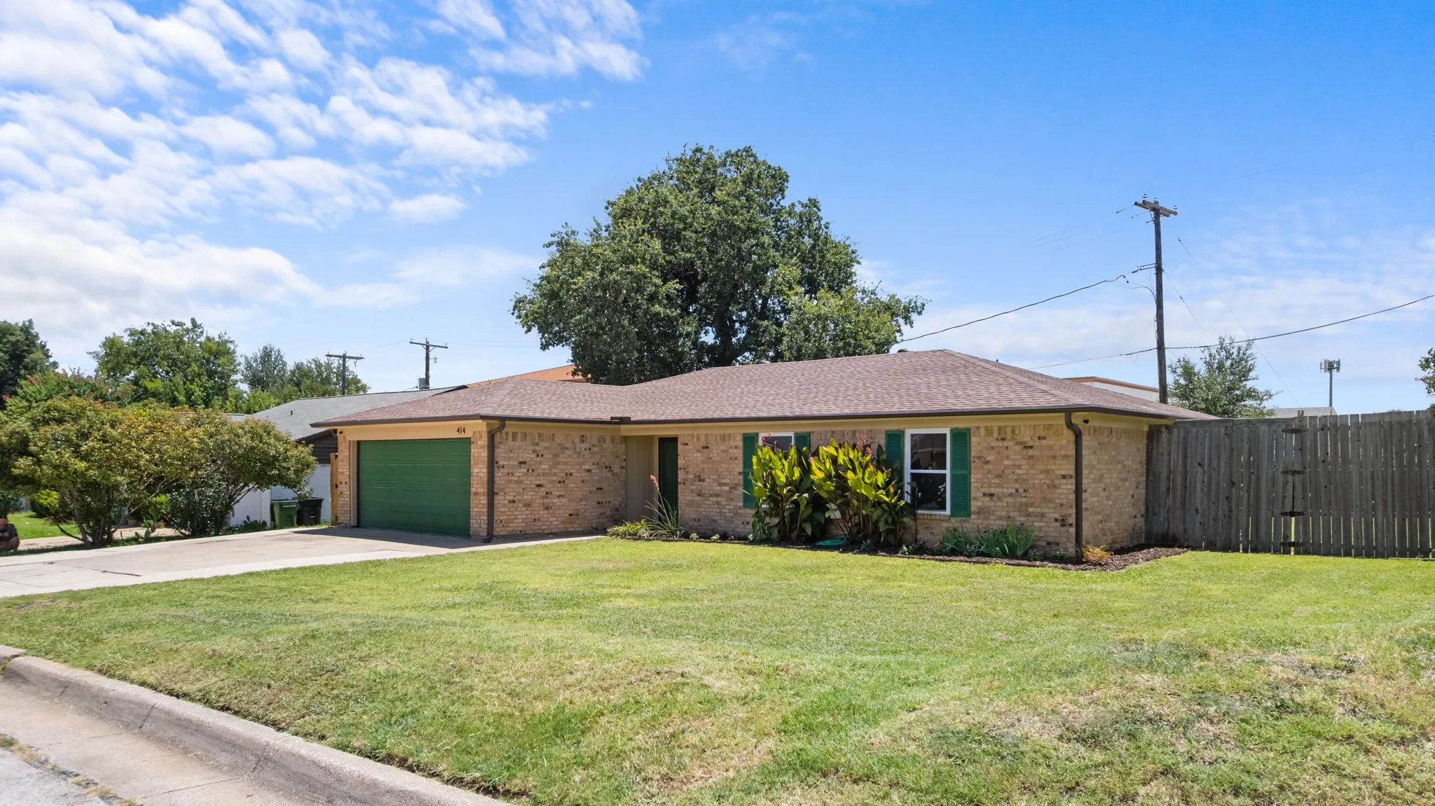 Brick exterior with a green garage door, a front yard with established landscaping, and a wood privacy fence