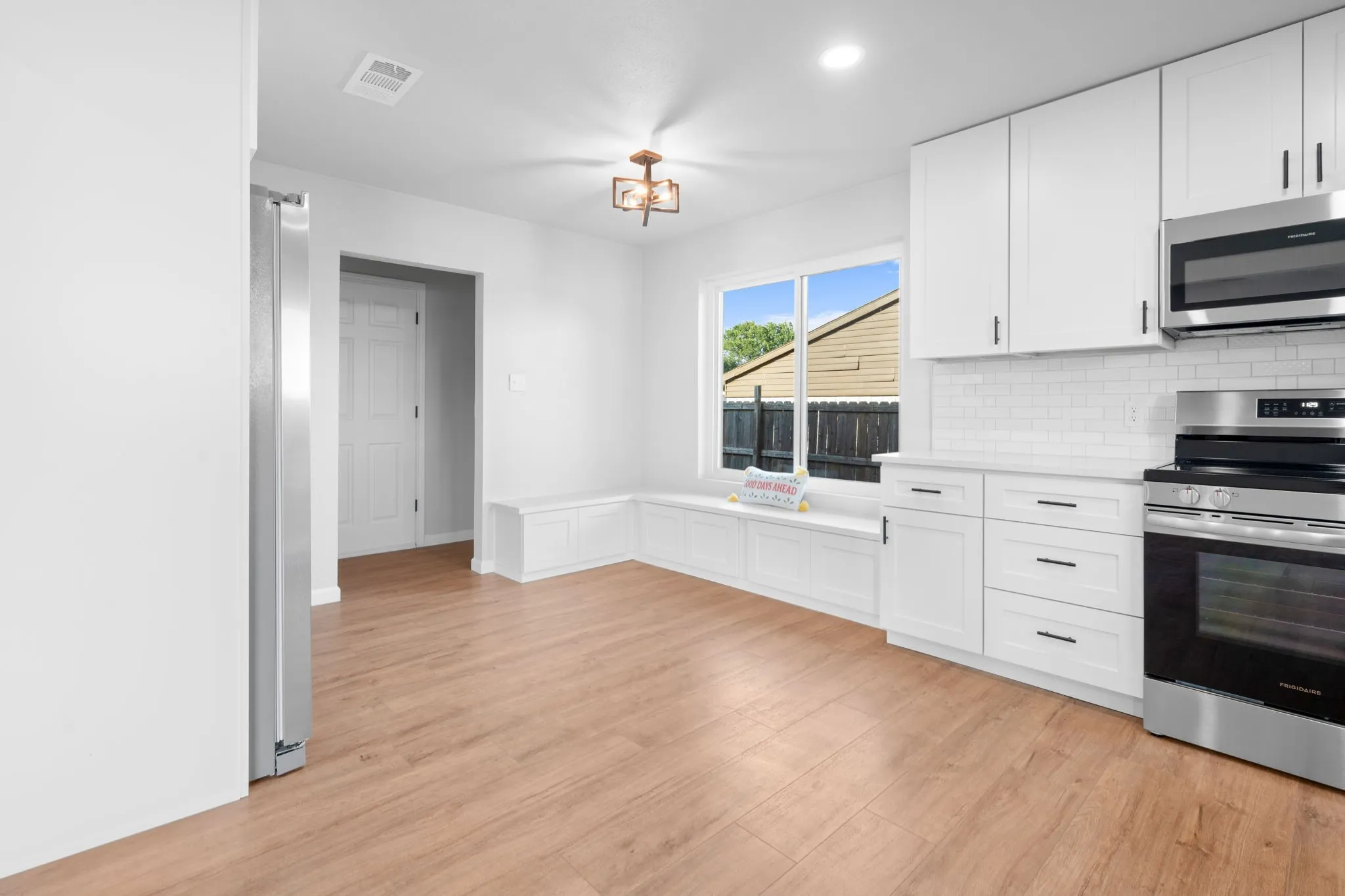 Kitchen featuring wood-finish flooring, white cabinetry, stainless steel appliances, and a built-in window bench