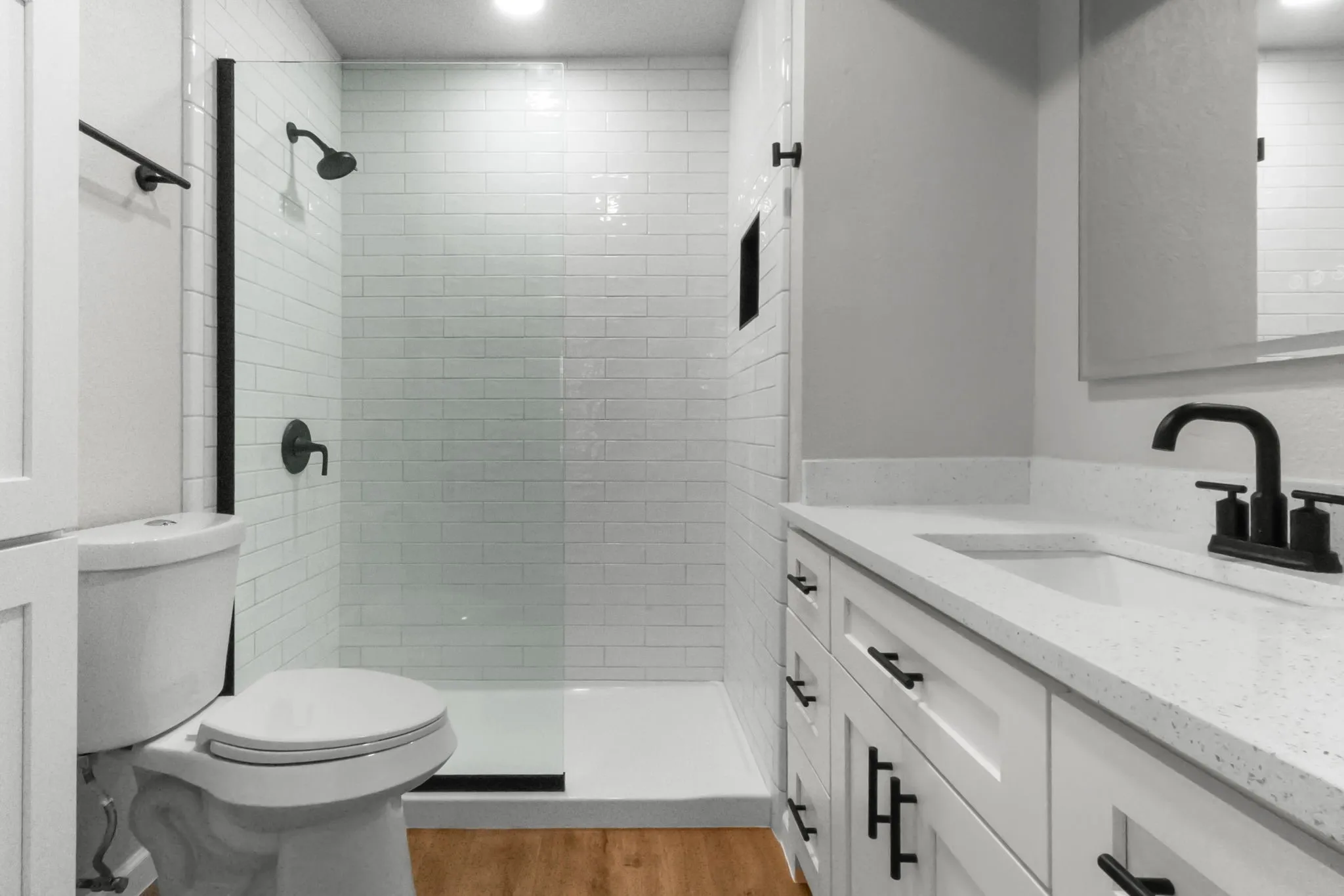 White subway tile shower with a clear glass enclosure, matte black fixtures, and a recessed niche