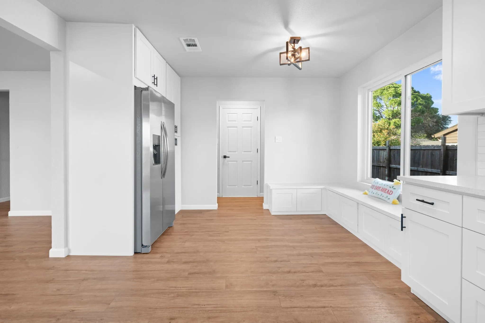 Wood-finish flooring throughout, white cabinetry with black hardware, built-in window seating with storage, and a contemporary ceiling fixture