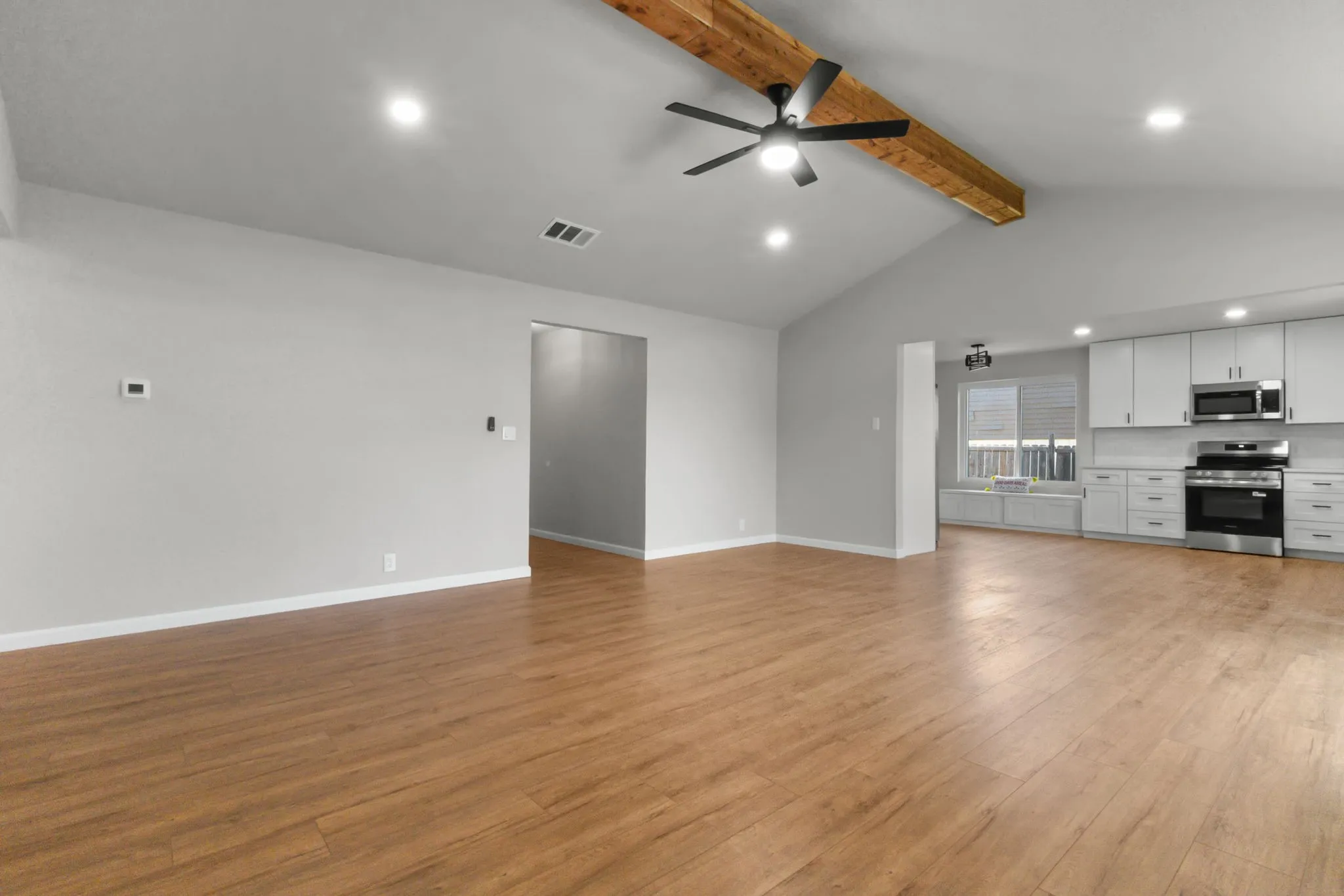 Vaulted ceiling with an exposed wood beam, recessed lighting, wood-finish flooring, white cabinetry, and stainless steel appliances