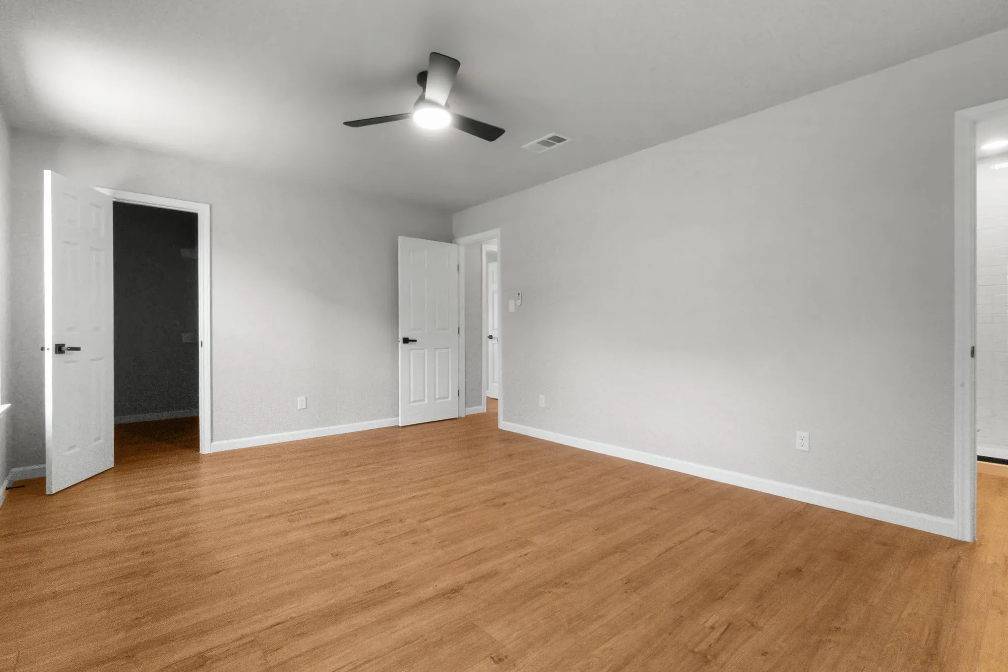 Spacious room featuring wood-finish flooring, light gray walls, white trim, and a ceiling fan with integrated lighting