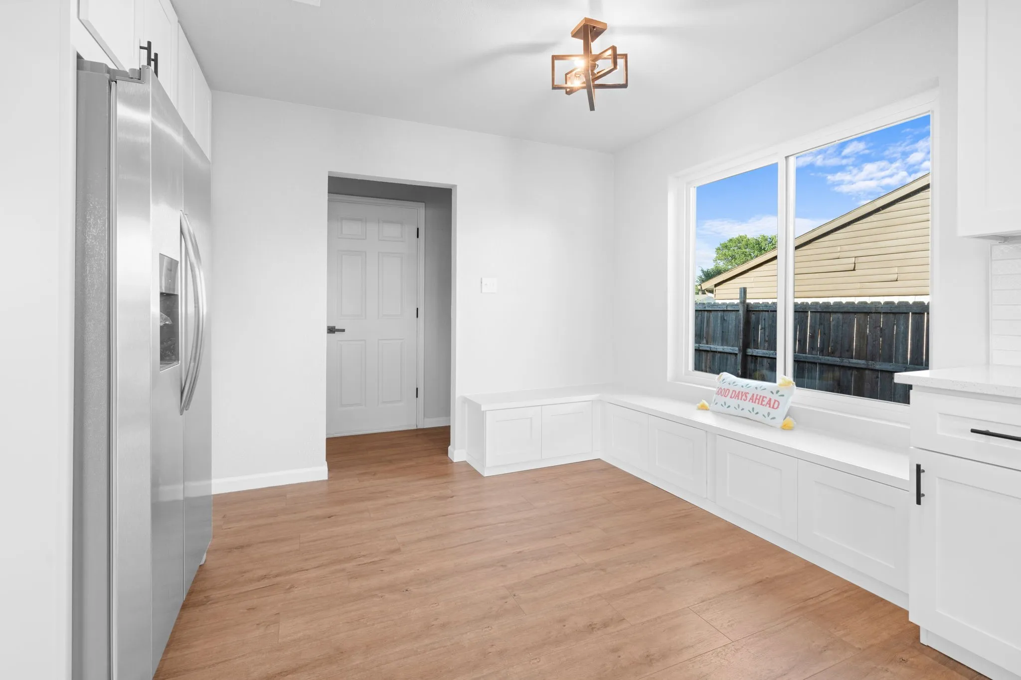 Stainless steel refrigerator, wood-finish flooring, white built-in bench seating, white cabinetry, and a modern ceiling light fixture