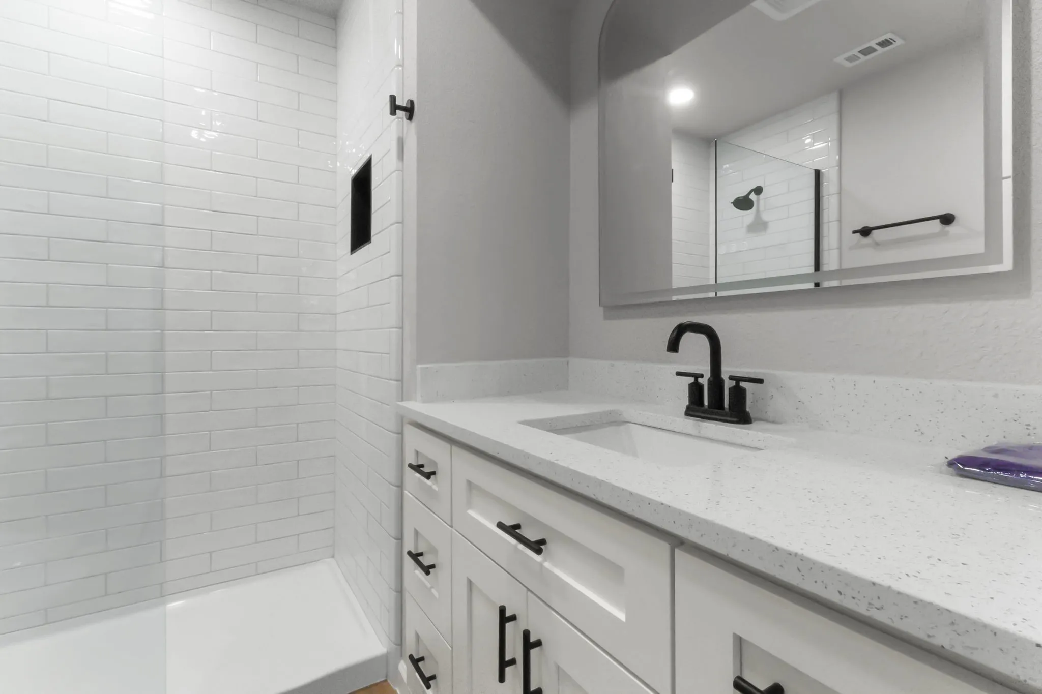 White subway tile shower with a built-in niche, a white vanity with shaker-style cabinetry, and a light-colored countertop with an integrated sink