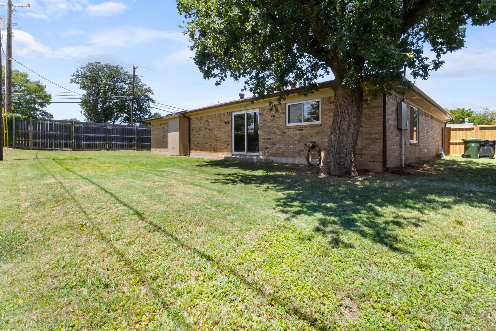 Expansive backyard with a manicured lawn, full privacy fencing, mature tree, and a brick exterior
