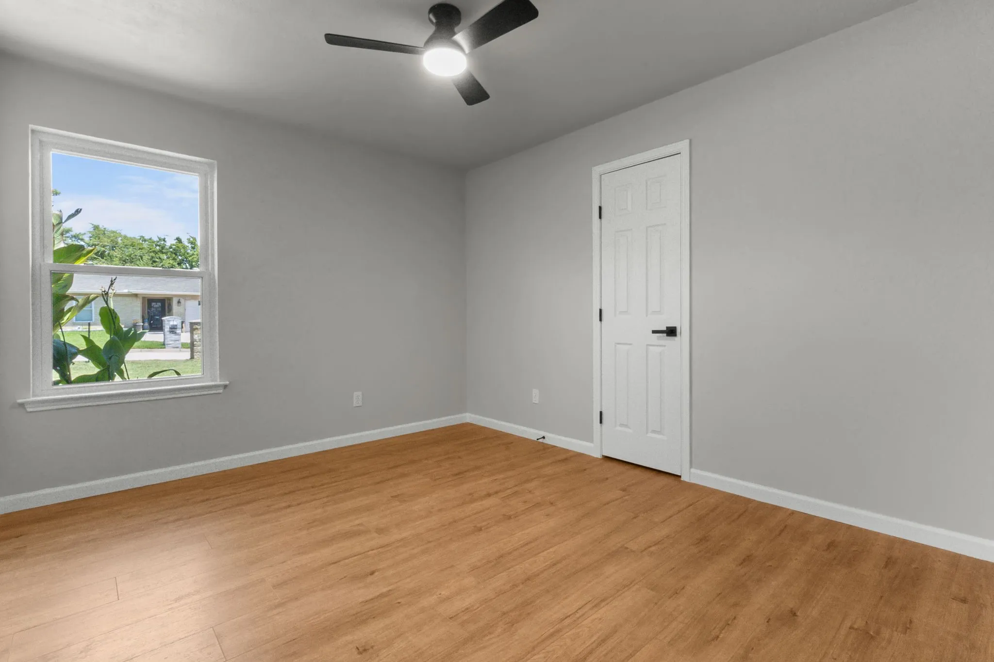 Wood-finish flooring, white trim, and a black ceiling fan with integrated lighting