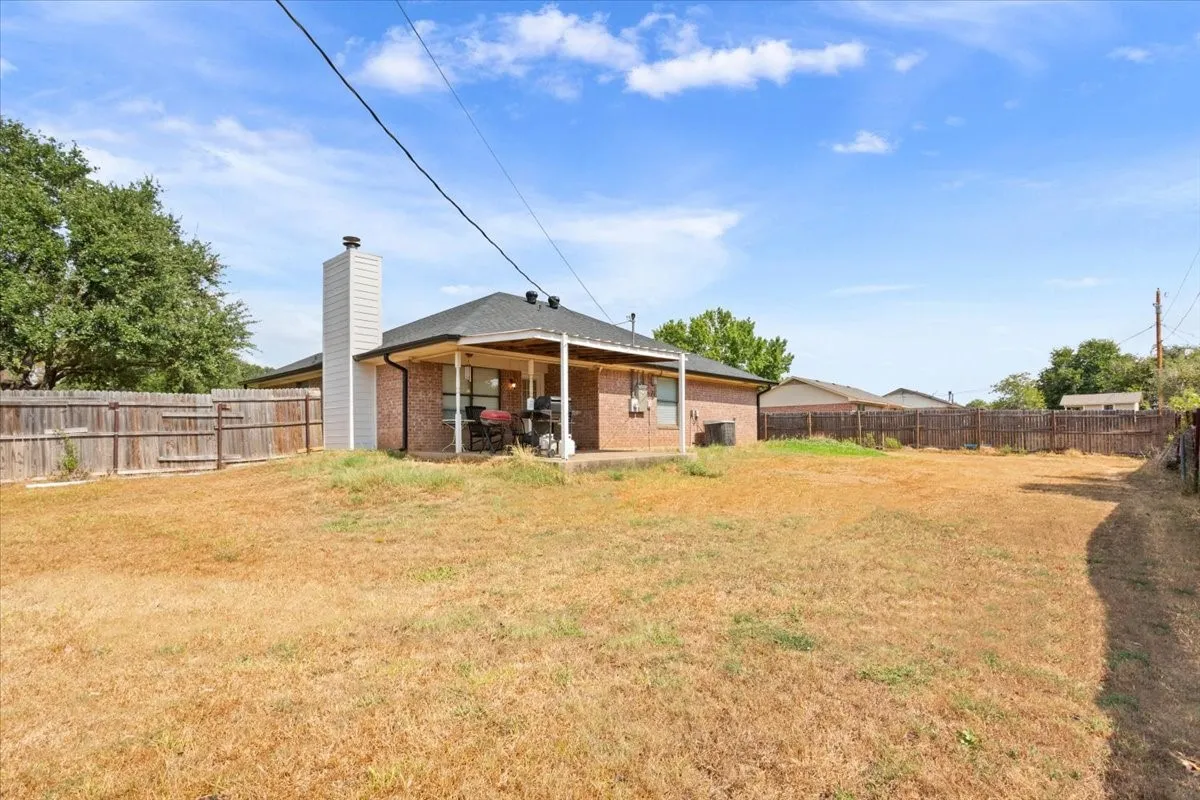 Expansive backyard featuring a covered patio, brick exterior, wood-paneled chimney, and full perimeter fencing