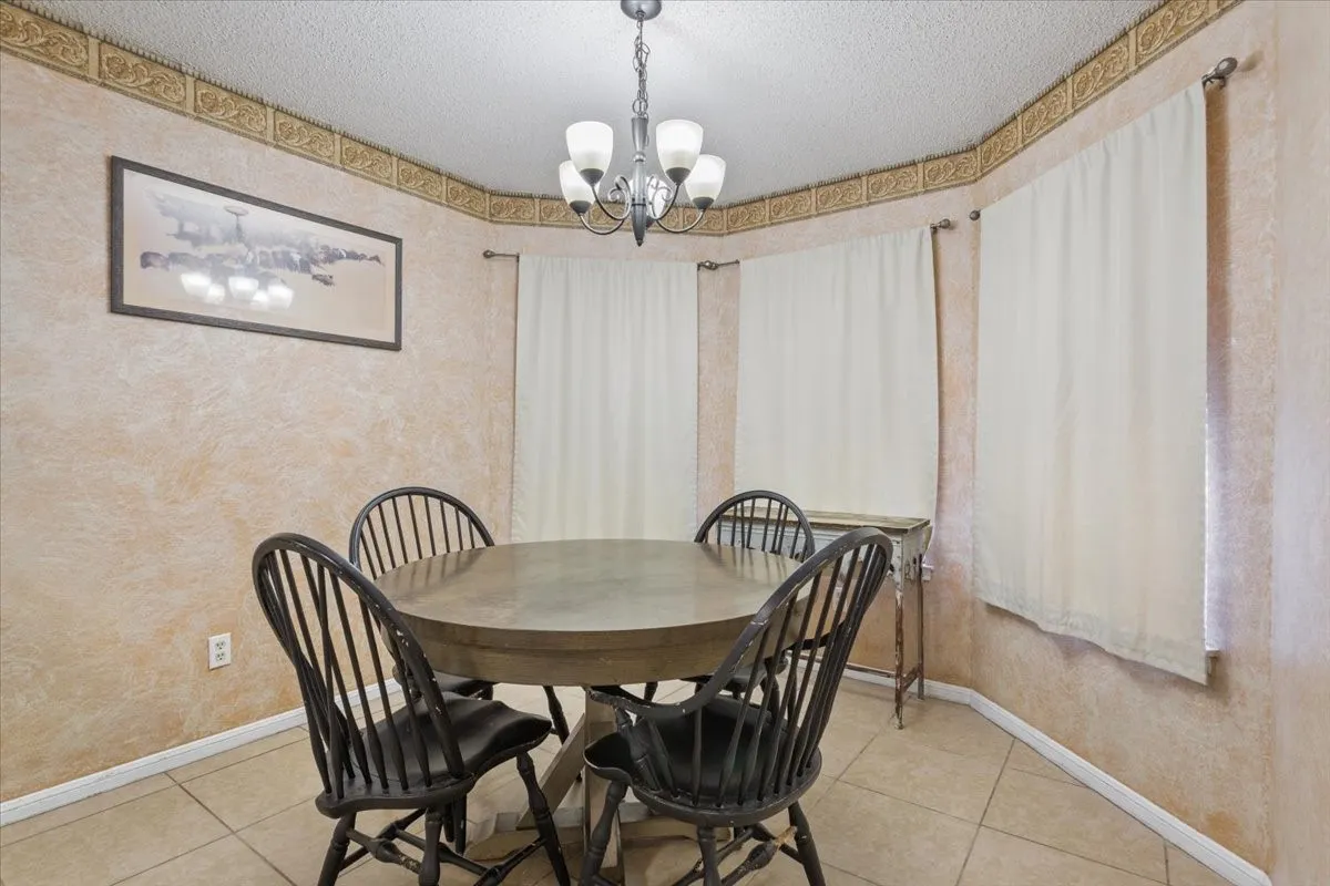 Bay window with multiple panels, tiled flooring, textured wall finish, decorative ceiling border, and a five-light chandelier