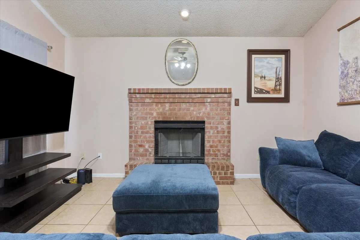 Brick fireplace with a black firebox and hearth, recessed ceiling lighting, and light-toned tile flooring
