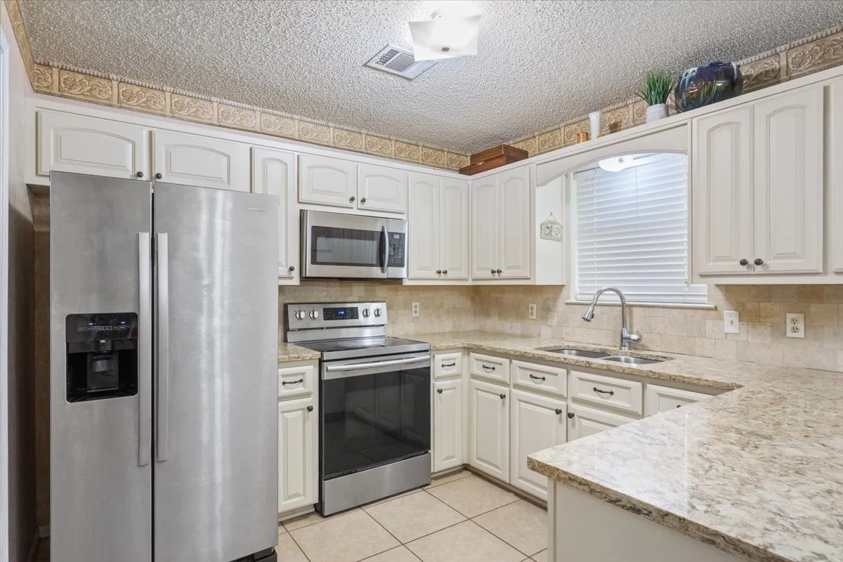 Kitchen featuring white cabinetry, stainless steel appliances, a double basin sink, and light-toned countertops