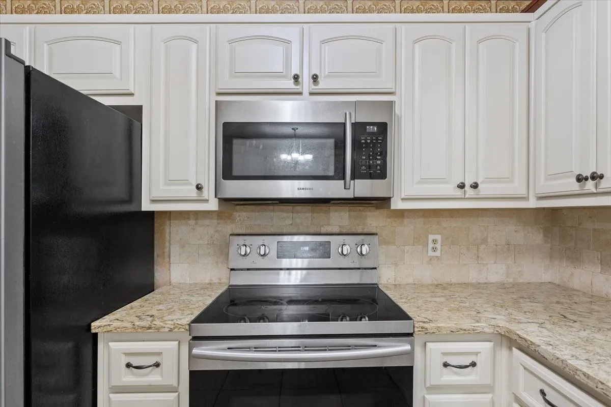White cabinetry with dark hardware, stone-look countertops, and a tiled backsplash