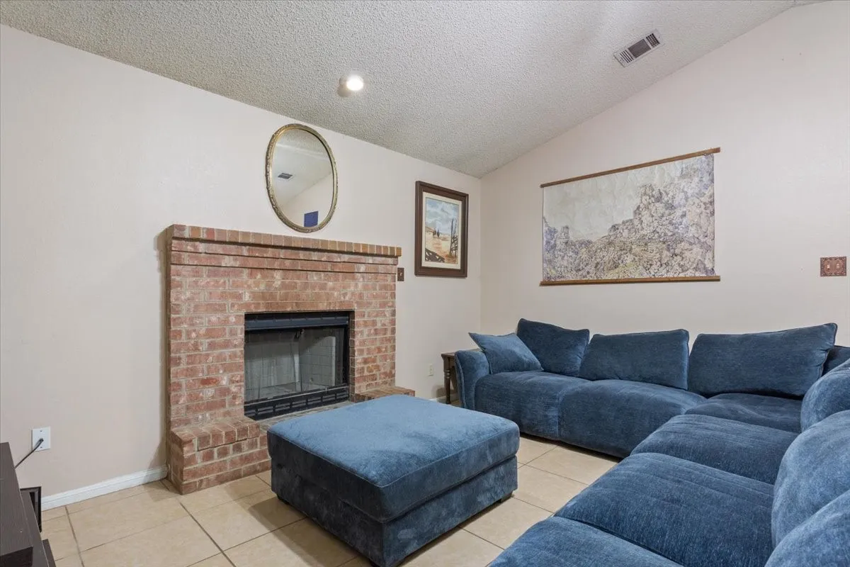 Brick fireplace with a black firebox, vaulted ceiling, recessed lighting, and tile flooring