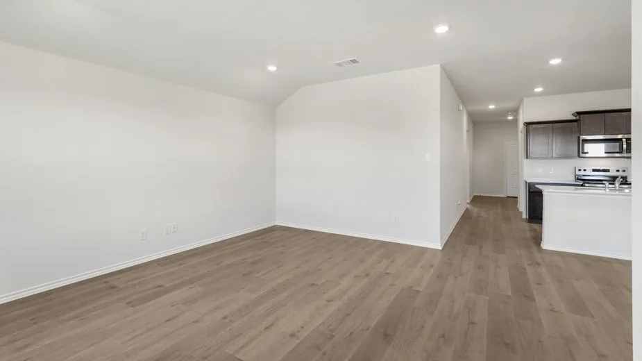 Open-concept living area featuring wood-finish flooring, recessed lighting, and a kitchen with dark wood cabinetry, a stainless steel microwave, and a stainless steel range