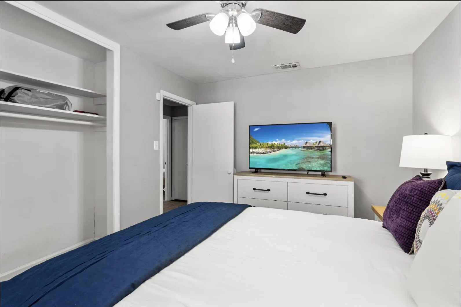 Recessed closet with shelving, ceiling fan with light fixture, light gray wall paint, white trim, and a white interior door