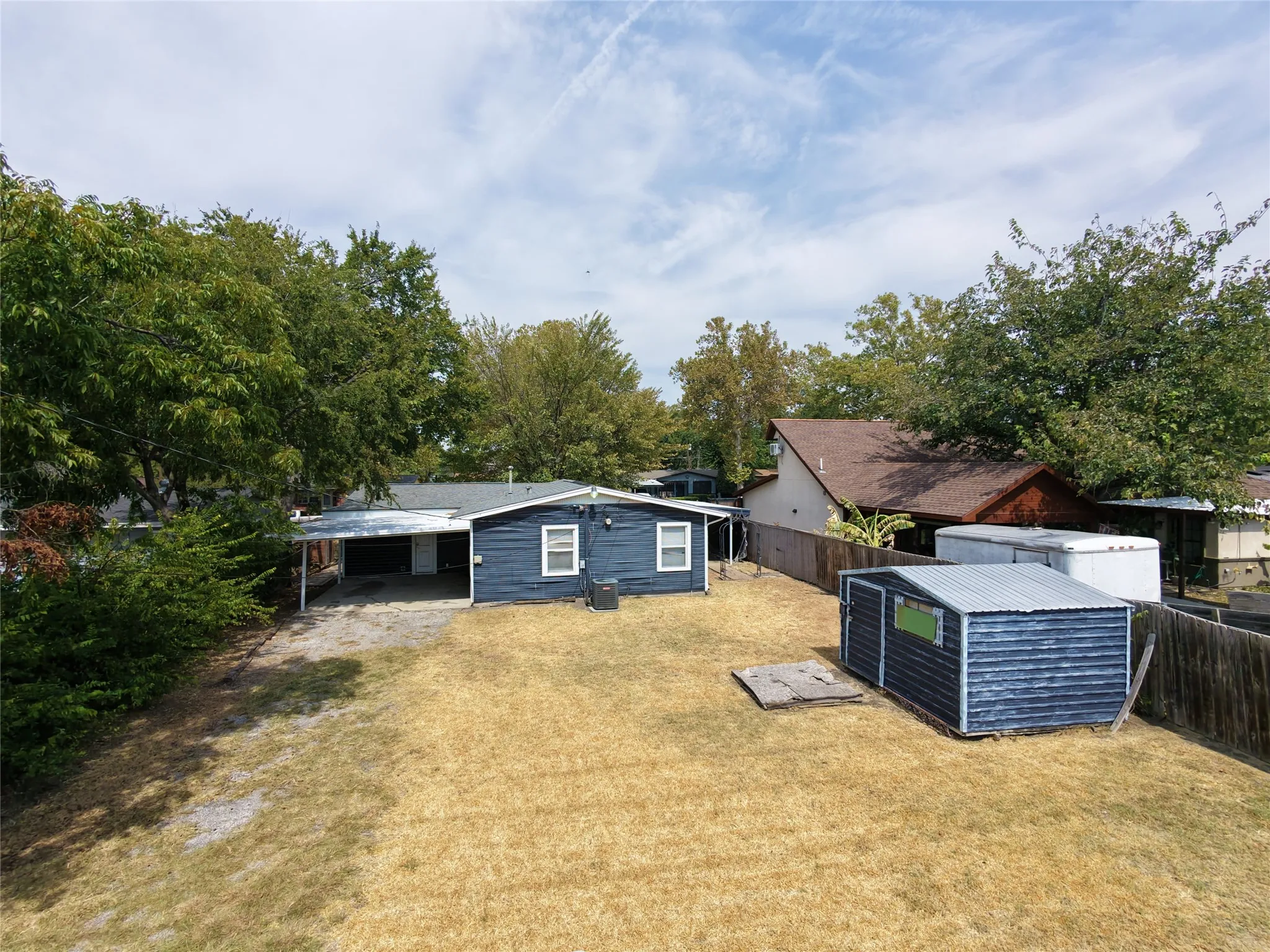 Blue-sided residence with white trim, a covered carport, and an outbuilding with a corrugated metal roof