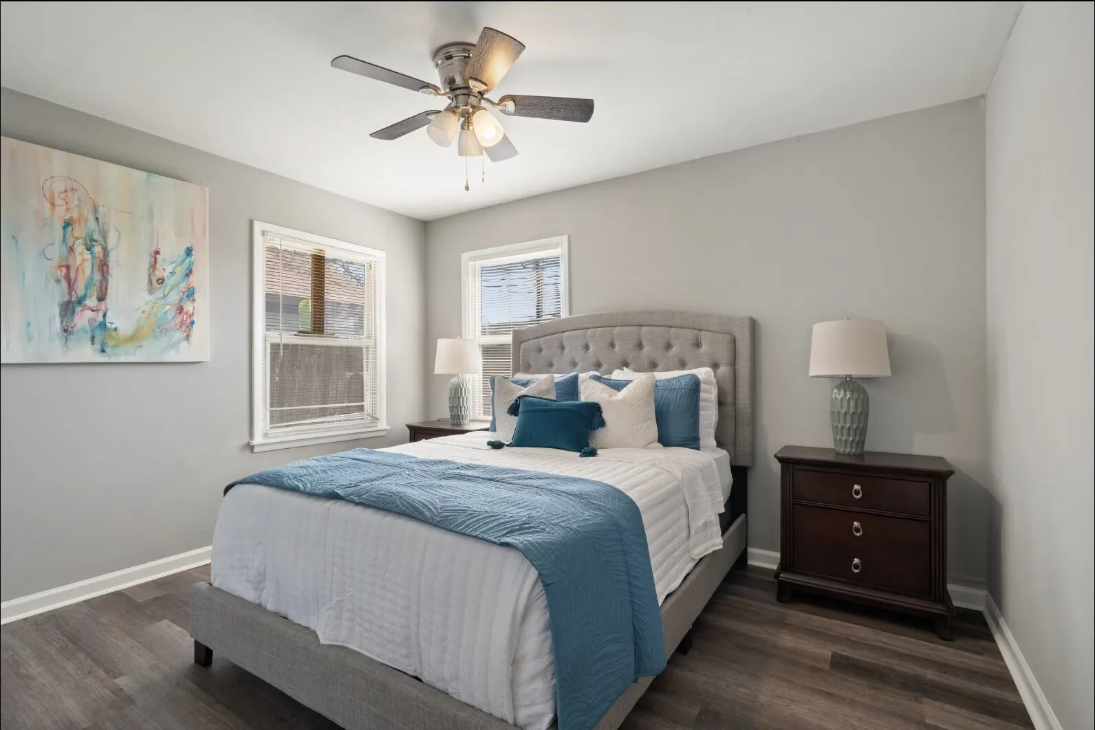 Wood-finish flooring, light grey wall paint, two windows with white trim, and a ceiling fan with integrated lighting