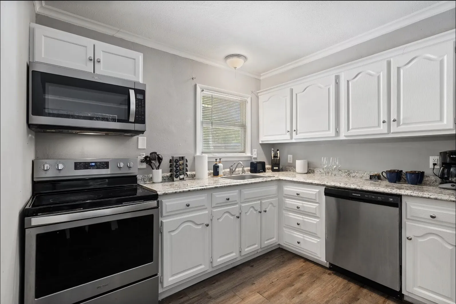 Kitchen featuring white cabinetry, light-toned countertops, stainless steel appliances, and wood-finish flooring